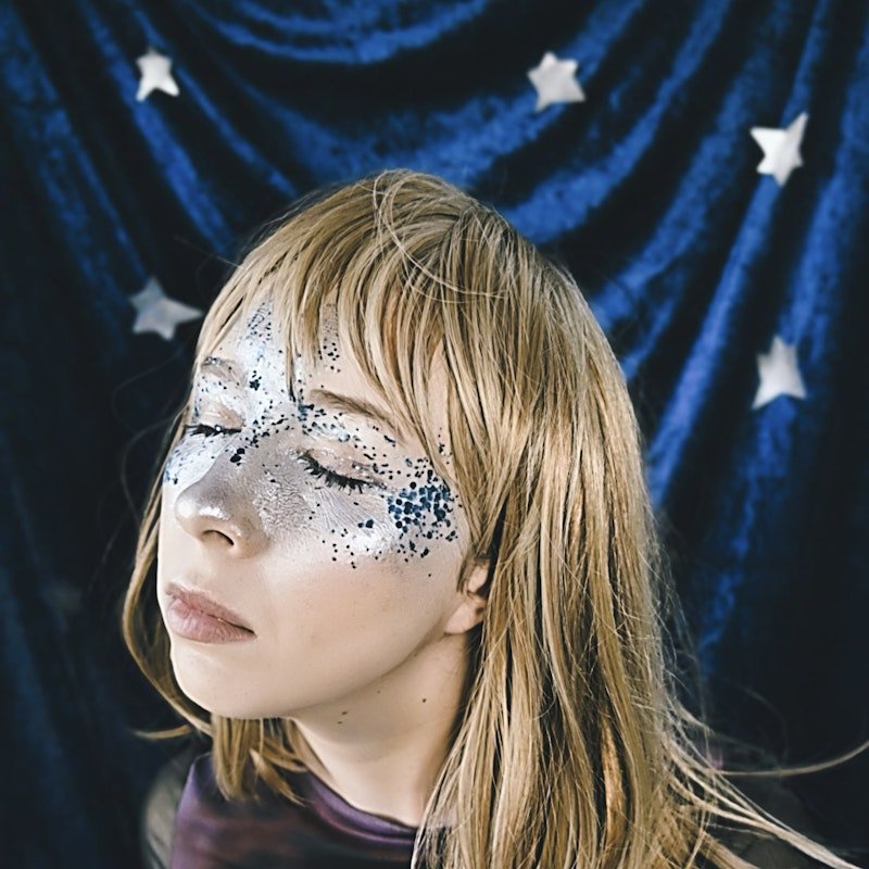 Young woman with closed eyes and glitter makeup, against a blue starry background.