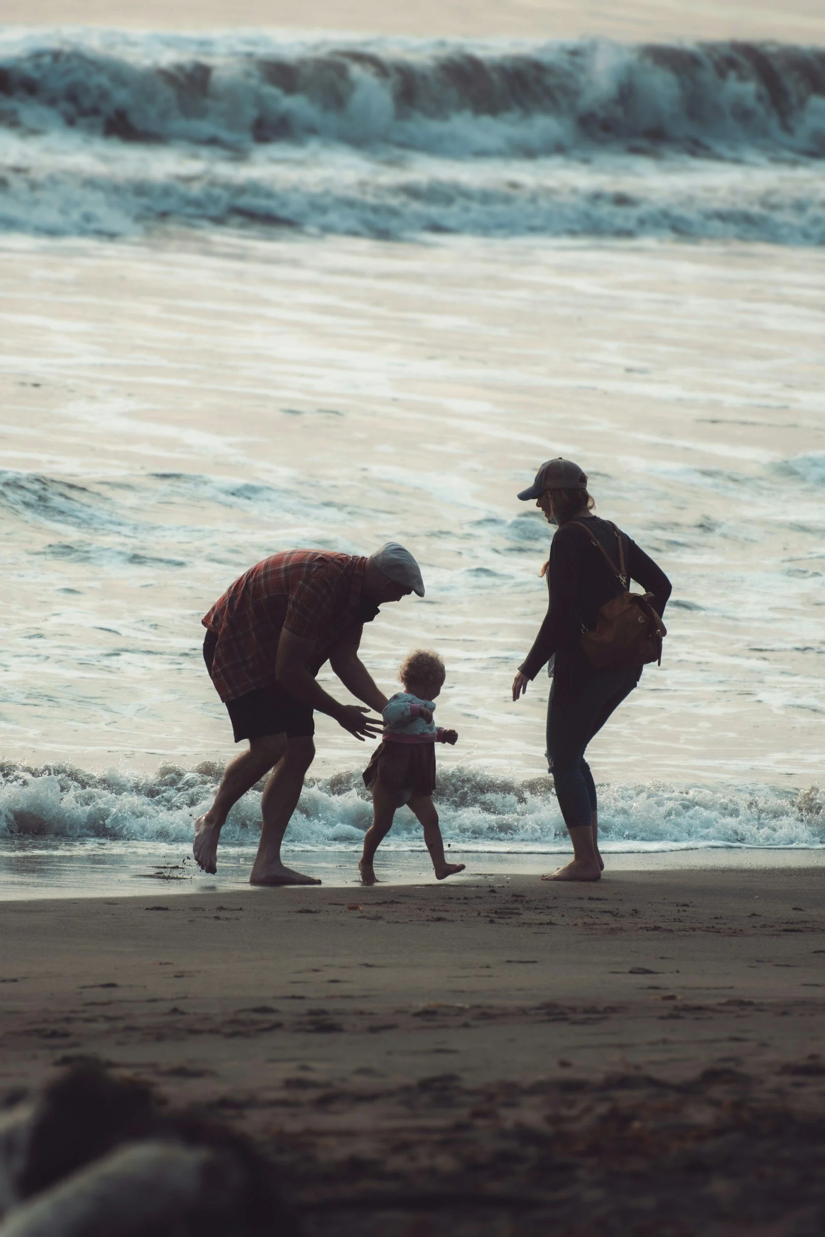 A family of four is playing on the beach near the water, with waves in the background during sunset or sunrise.