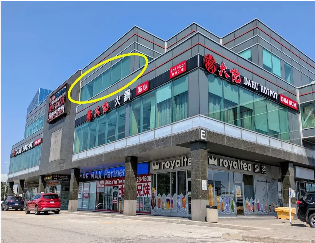 A modern multi-story commercial building with signs indicating a hotpot restaurant, a dental clinic, and a beverage store. The building has large windows, and there are cars parked in front, with a clear blue sky overhead.