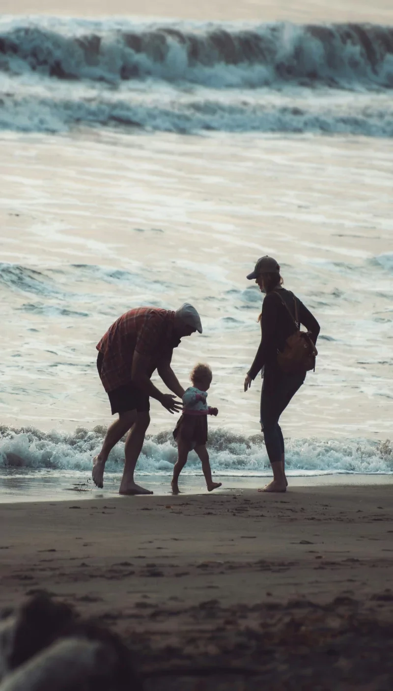 A family of four is playing on the beach near the water, with waves in the background during sunset or sunrise.