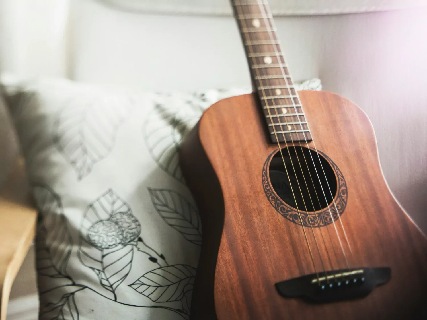 Close-up of an acoustic guitar resting on a bed with a striped, multi-colored blanket.