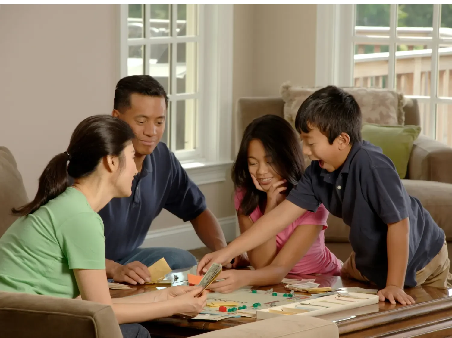 A family of four smiling and interacting warmly while playing a board game together in a comfortable living room.