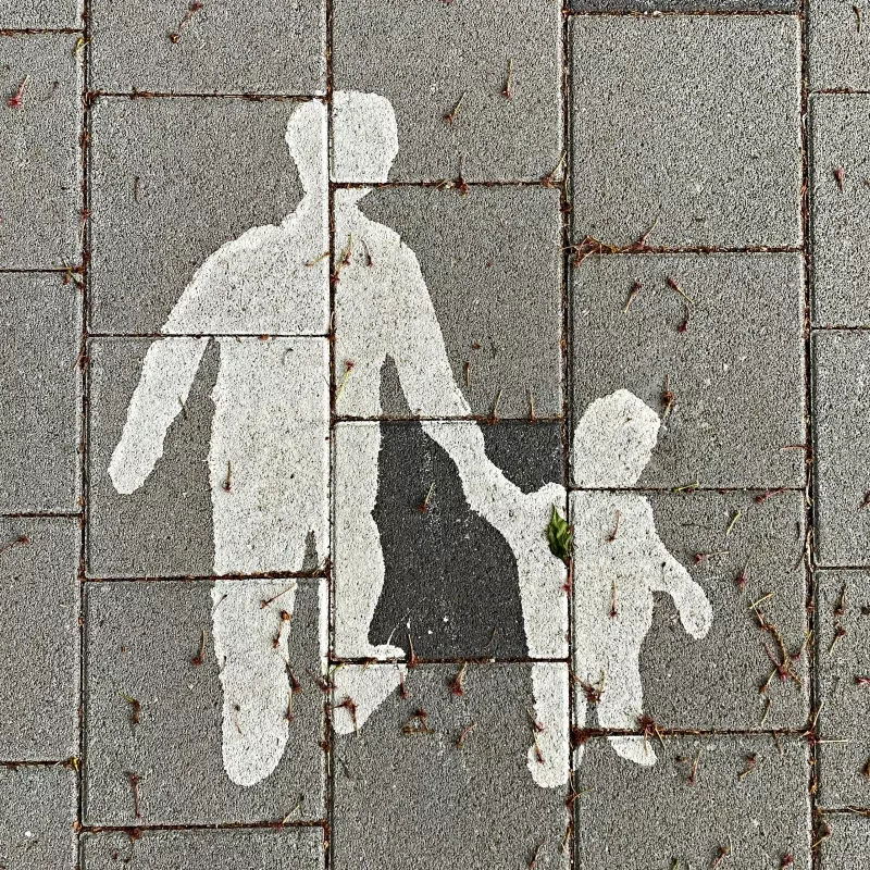 A sidewalk with a painted symbol of a person walking, made of white paint on grey bricks, with some small twigs and leaves scattered around.