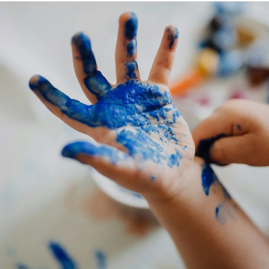 Close-up of a person's hand with blue paint splattered on fingers and palm.