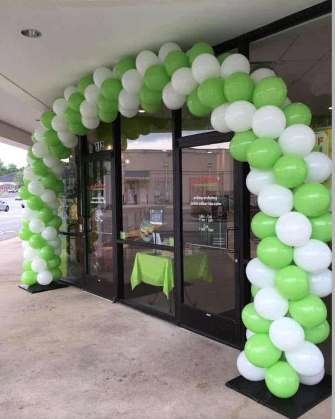 Green and white balloon arch over the entrance of a storefront.