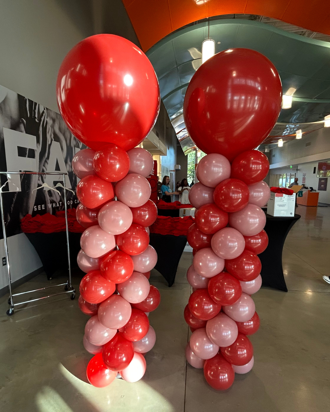 Two classic balloon columns with large red balloon tops and smaller red and pink balloons stacked underneath, set up indoors.