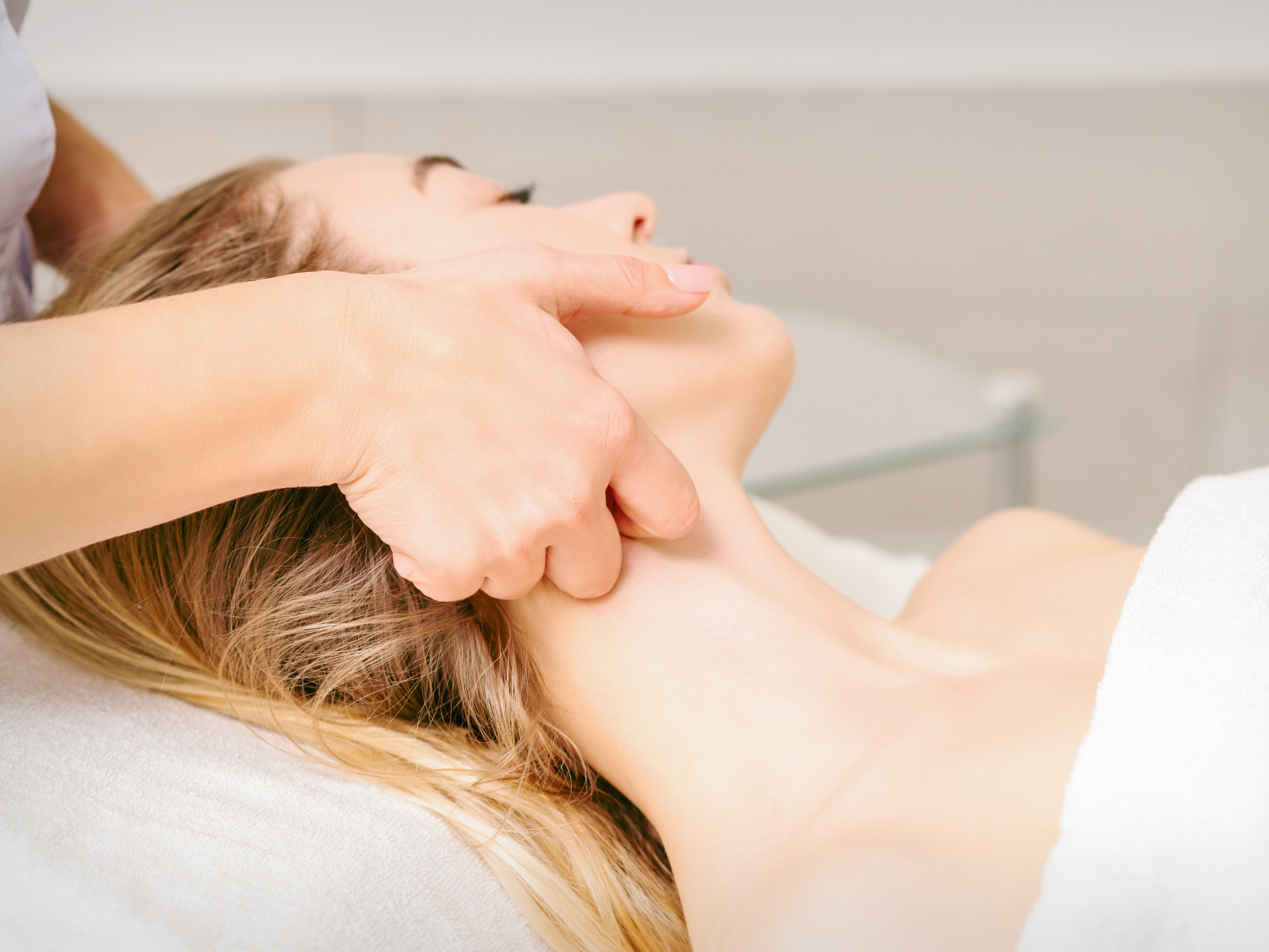 A woman receiving a facial massage or treatment from a therapist in a spa or clinic setting.