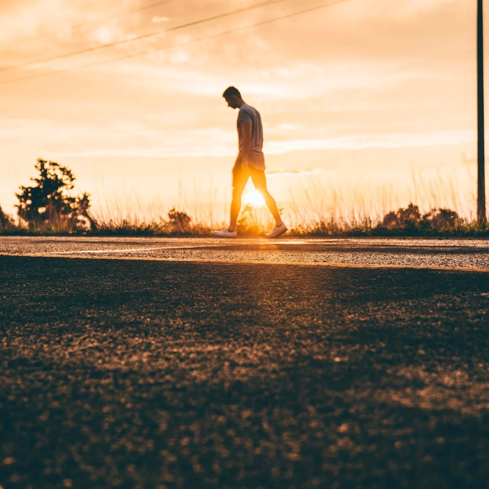 A person walking along a road at sunset, with the sun low in the sky casting a warm glow.