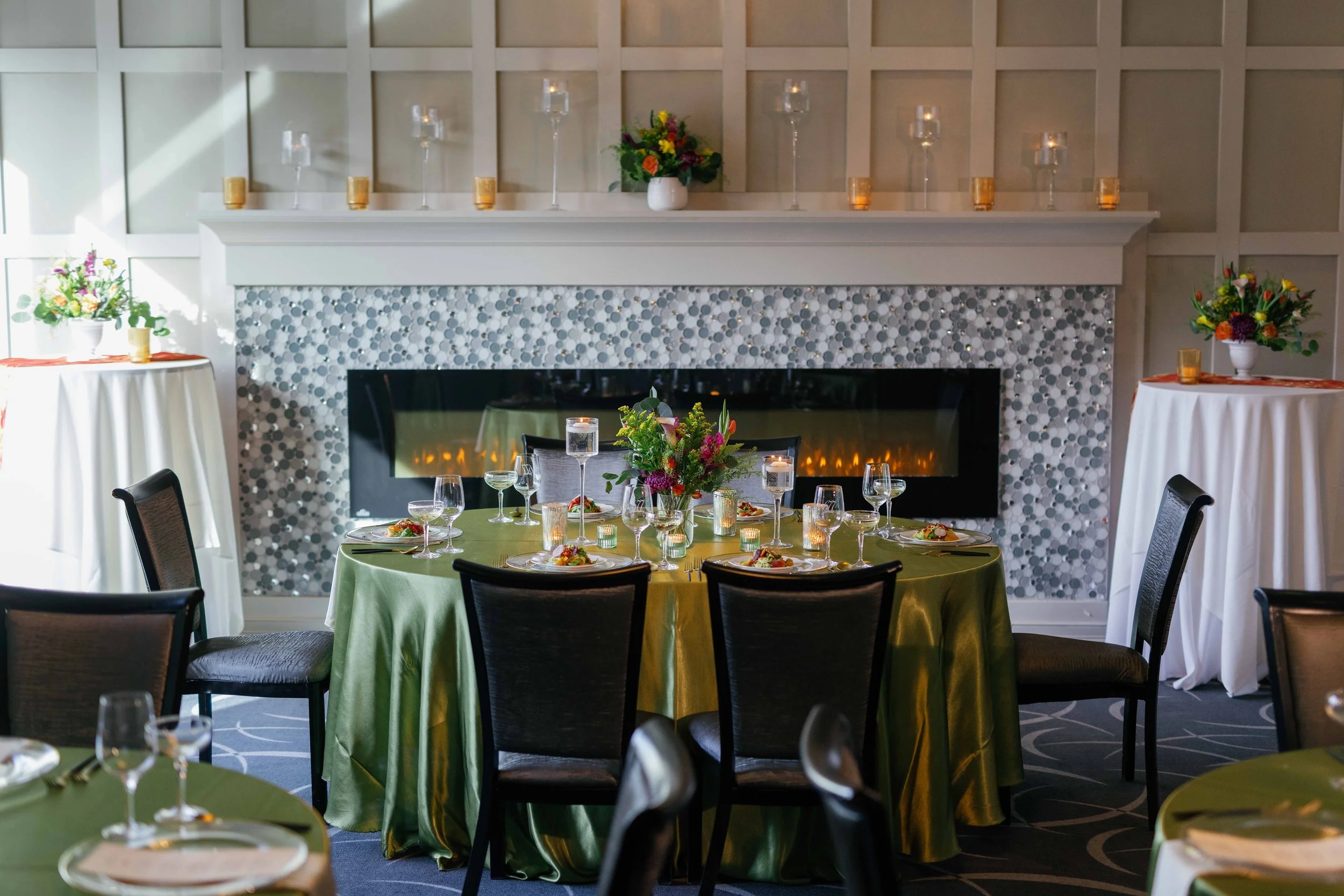 A decorated dining room with a fireplace, floral arrangements, and tables set for a formal event.