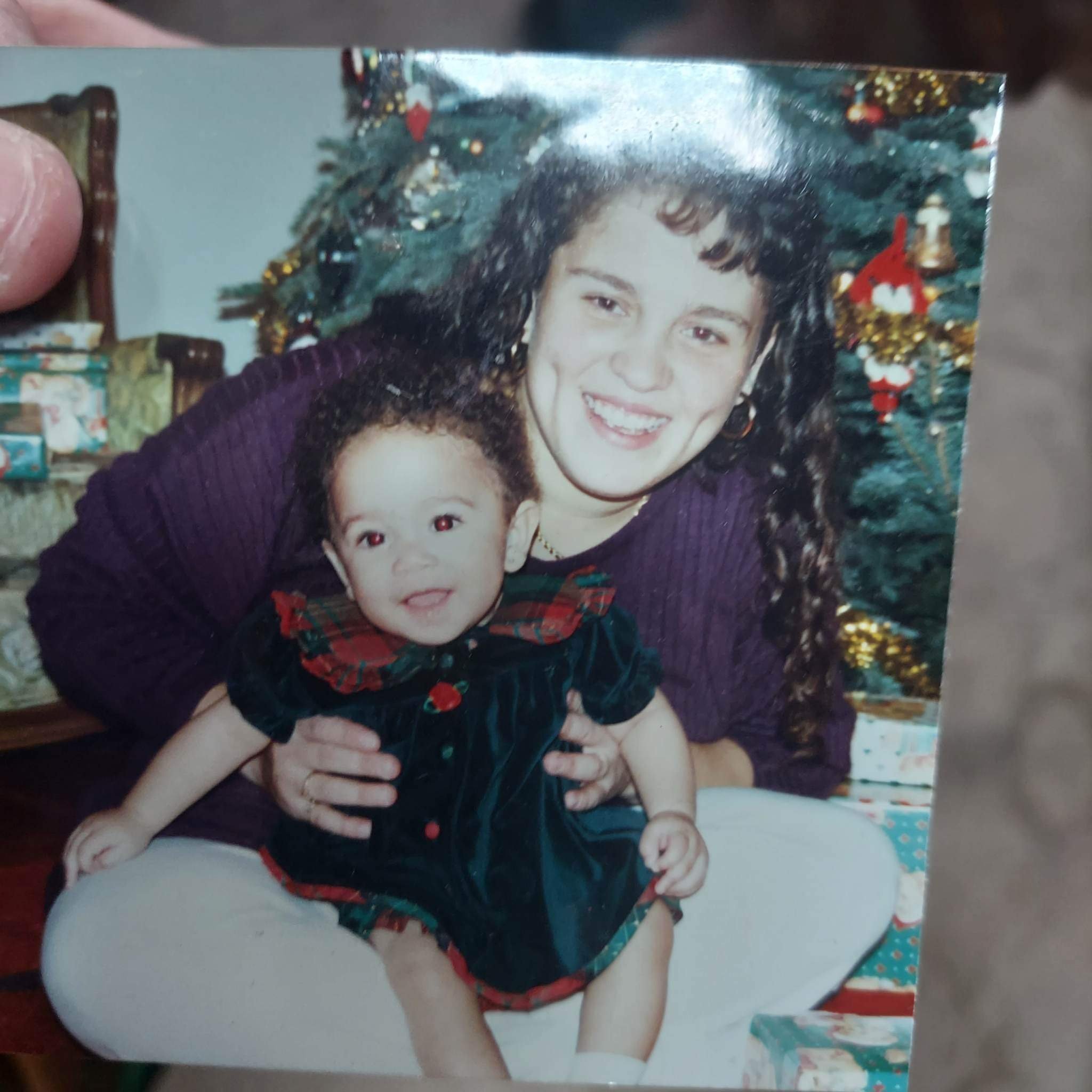 A woman and a young girl in front of a decorated Christmas tree with presents in the background.