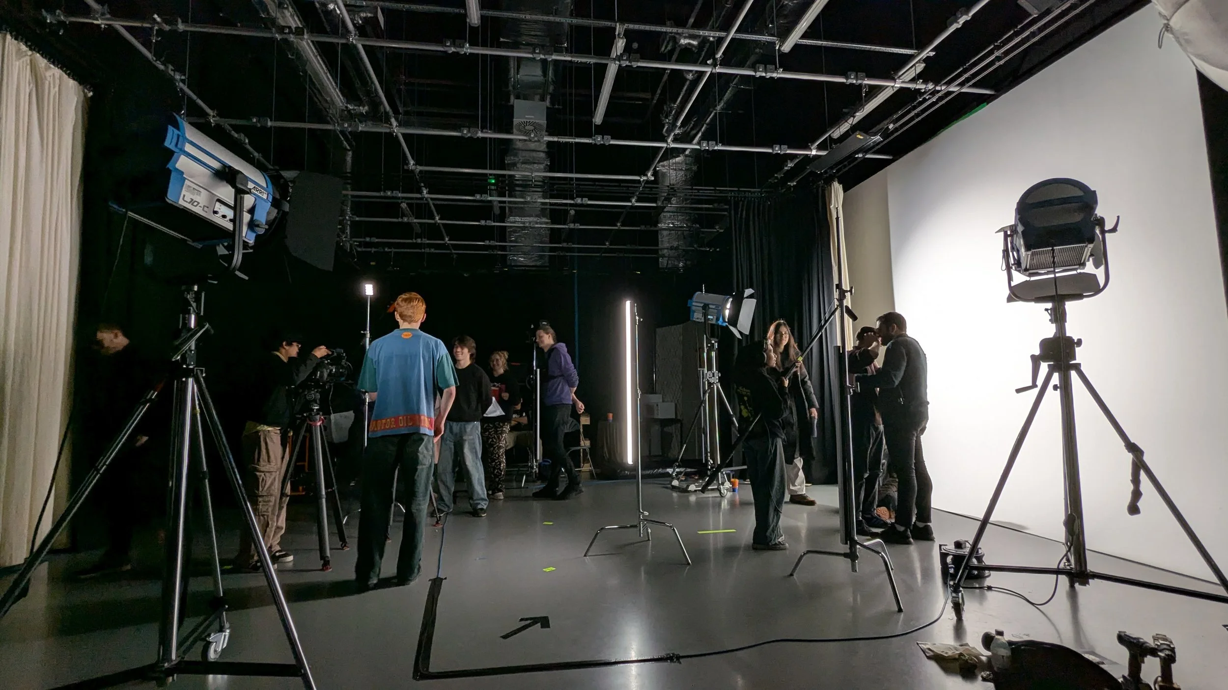 People working on a film or photo shoot with lighting and camera equipment in a studio with a white backdrop.