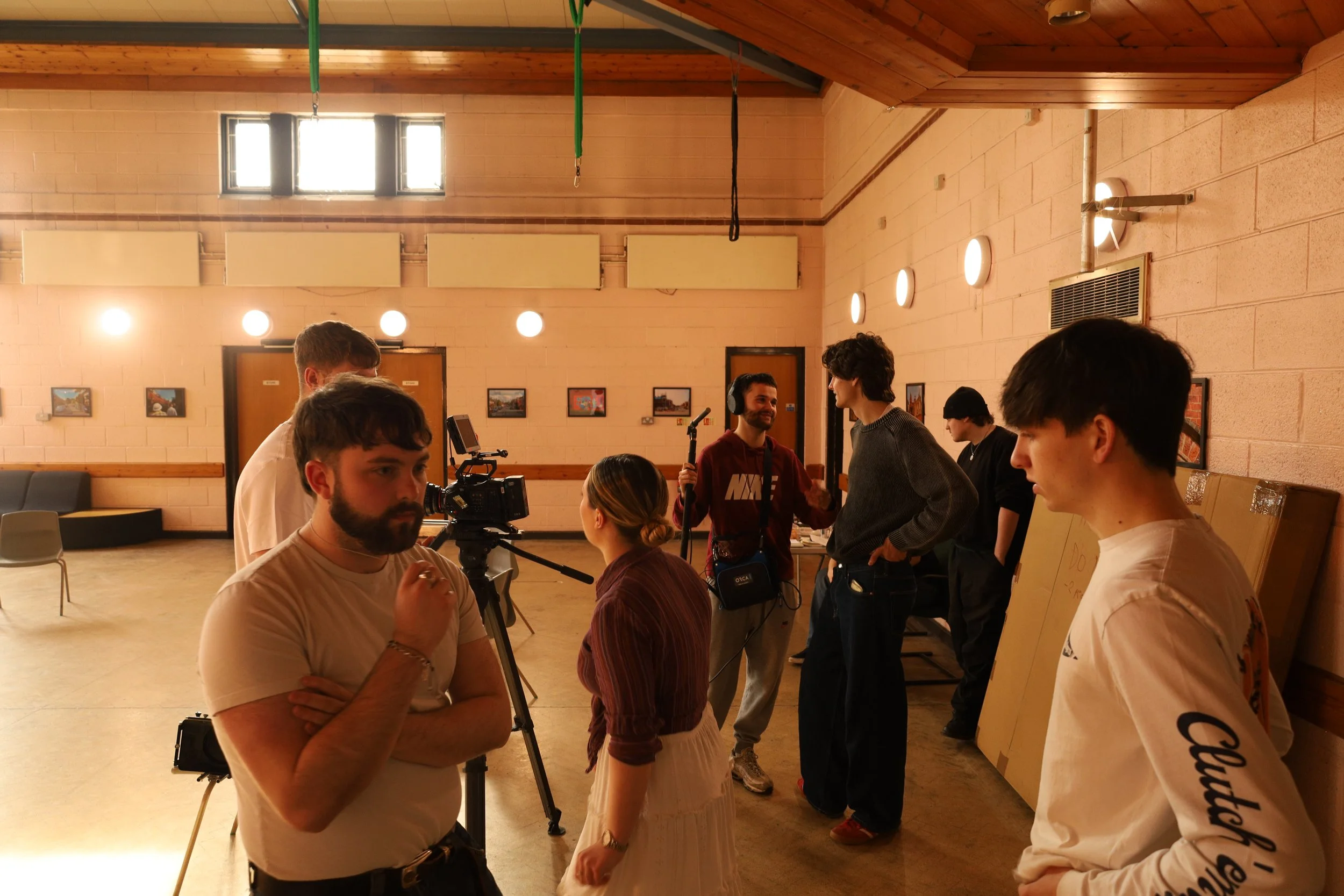 People working on film production in a studio, with a camera and crew members engaged in conversation.