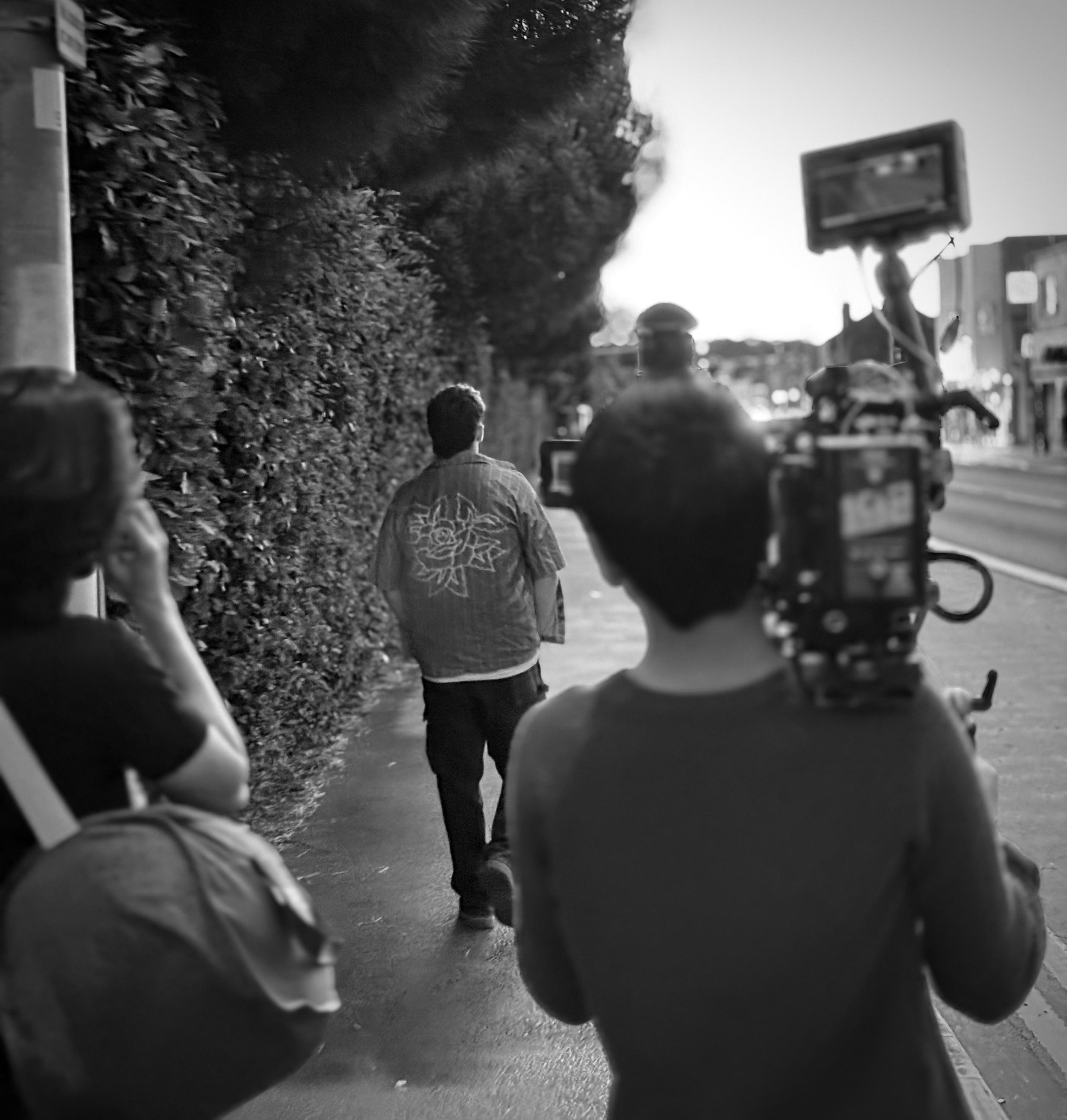 Filming a man walking on a sidewalk with a camera crew capturing footage in black and white.