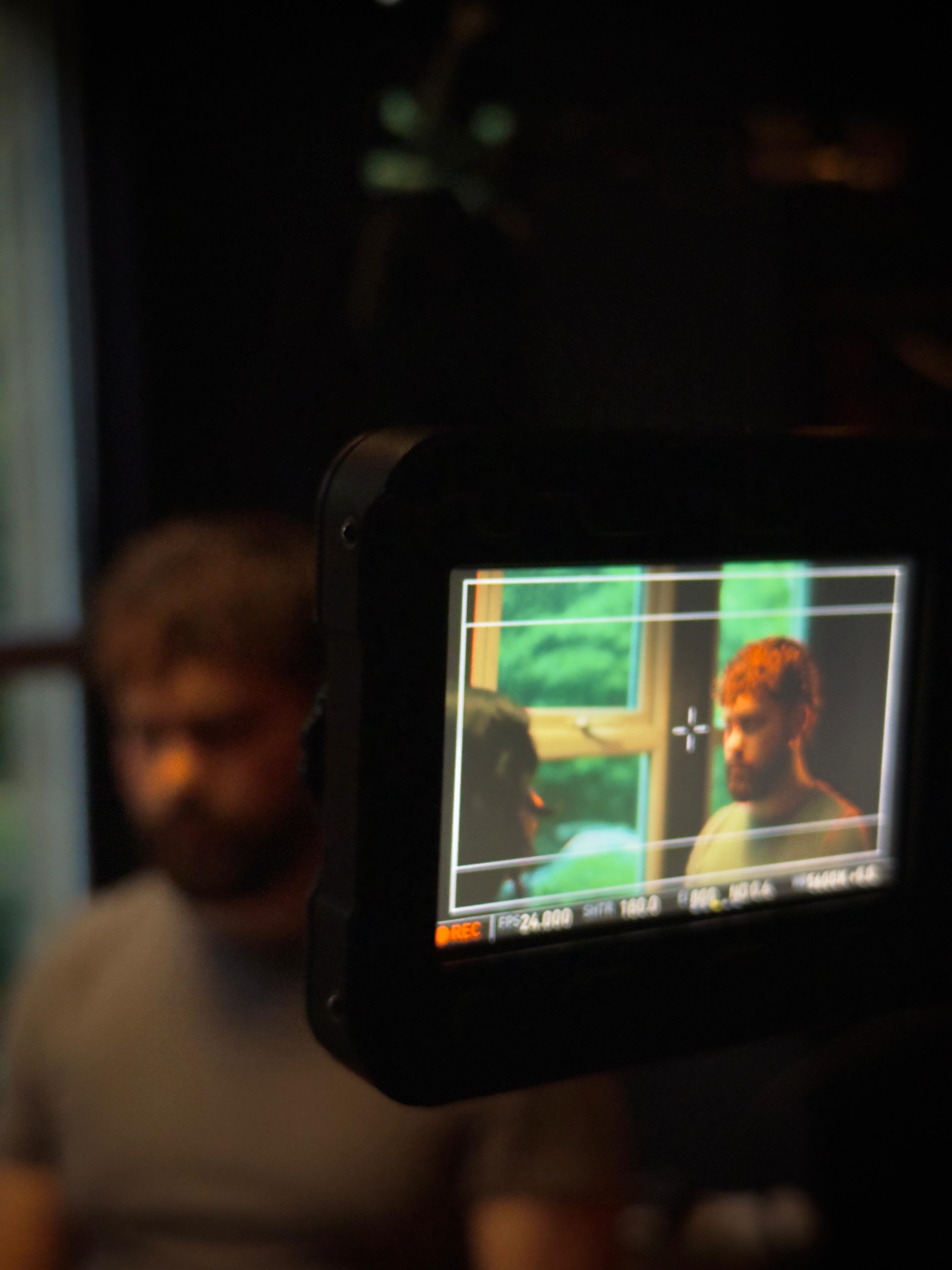 A camera screen shows two people having a conversation indoors with a window in the background.