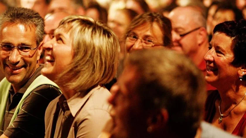 A group of people sitting in an audience, smiling and laughing during an event.