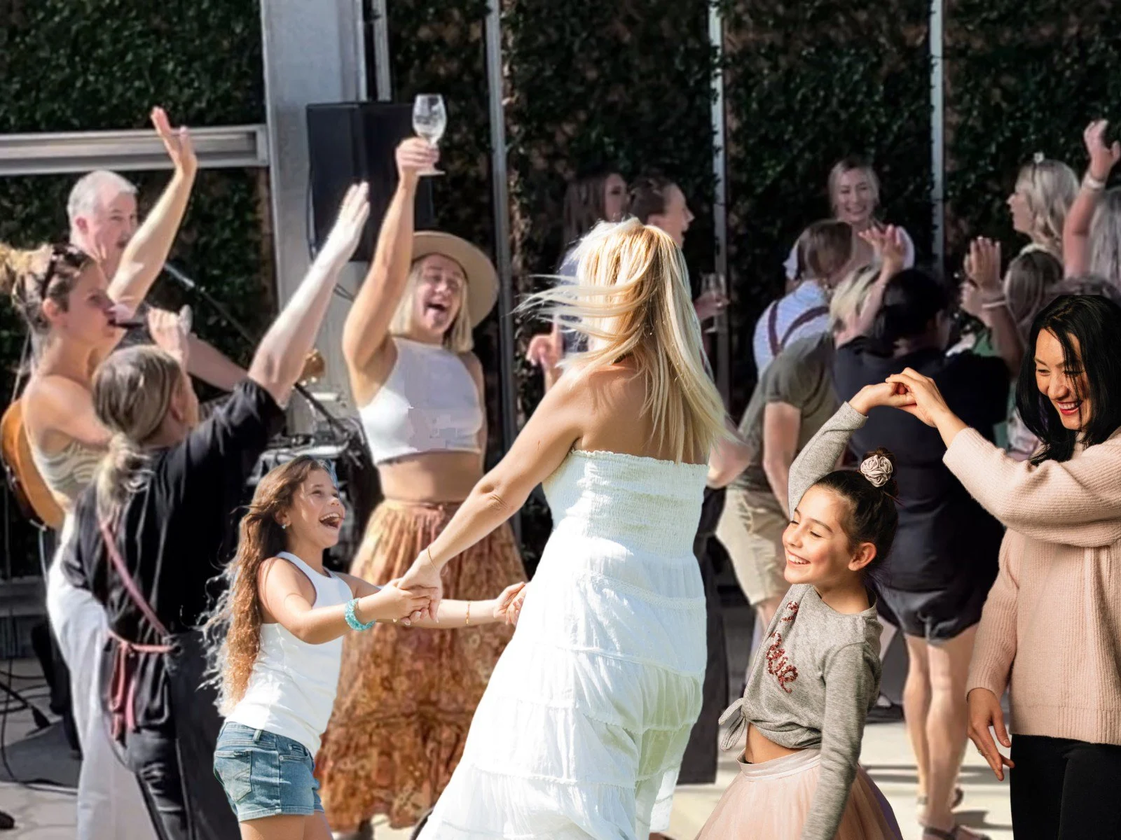 People dancing and celebrating outdoors, with women and children smiling, holding hands, and raising their arms.