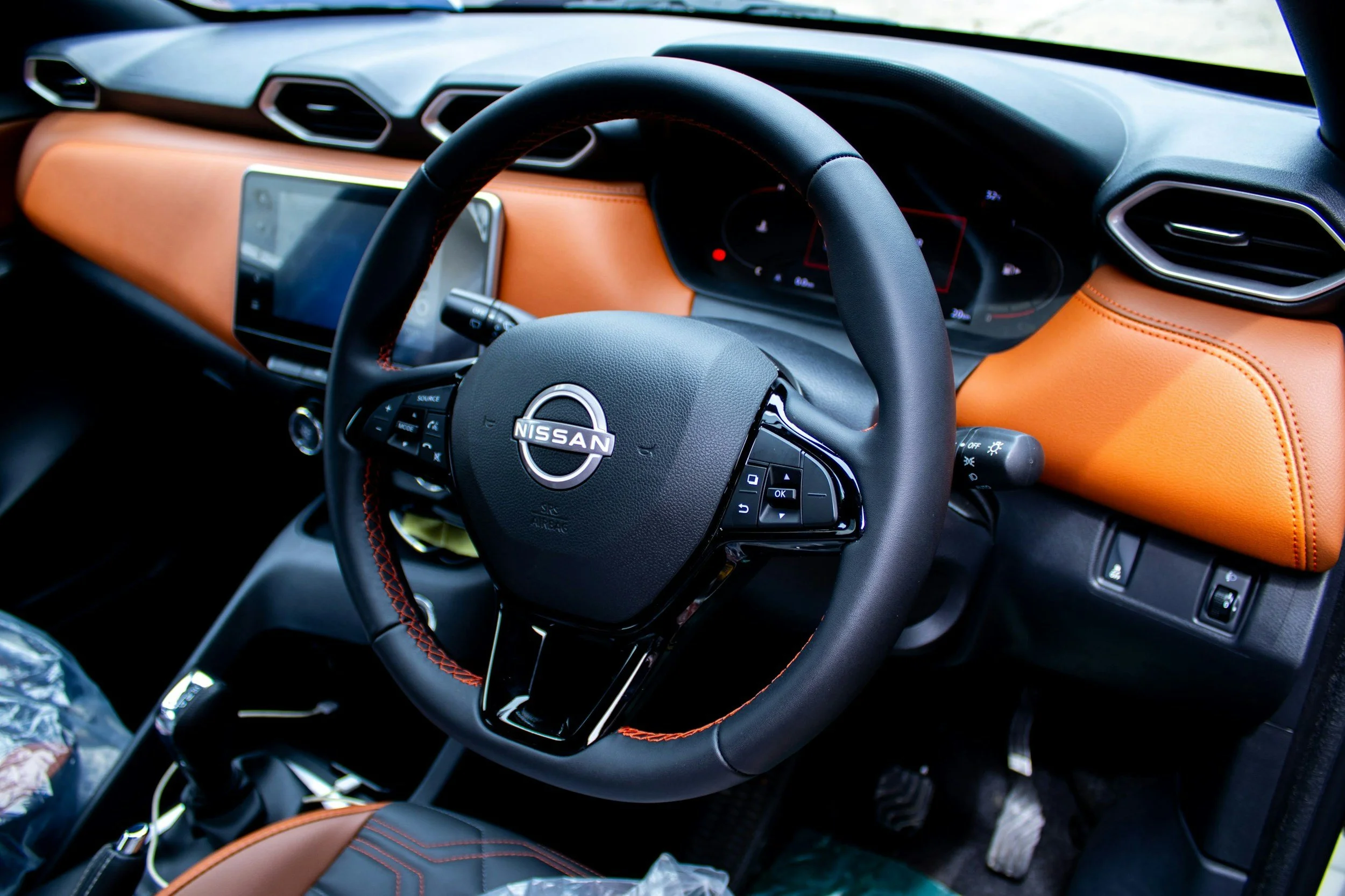 The interior of a Nissan vehicle featuring a black steering wheel with mounted controls, an orange dashboard with diamond stitching on the seats, and a digital instrument cluster.