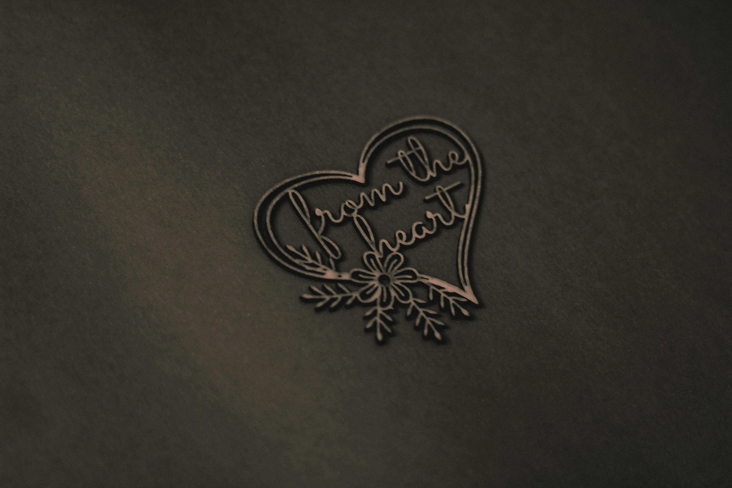 Embossed heart with the words 'from the heart' inside, decorated with a floral pattern underneath, on a dark background.
