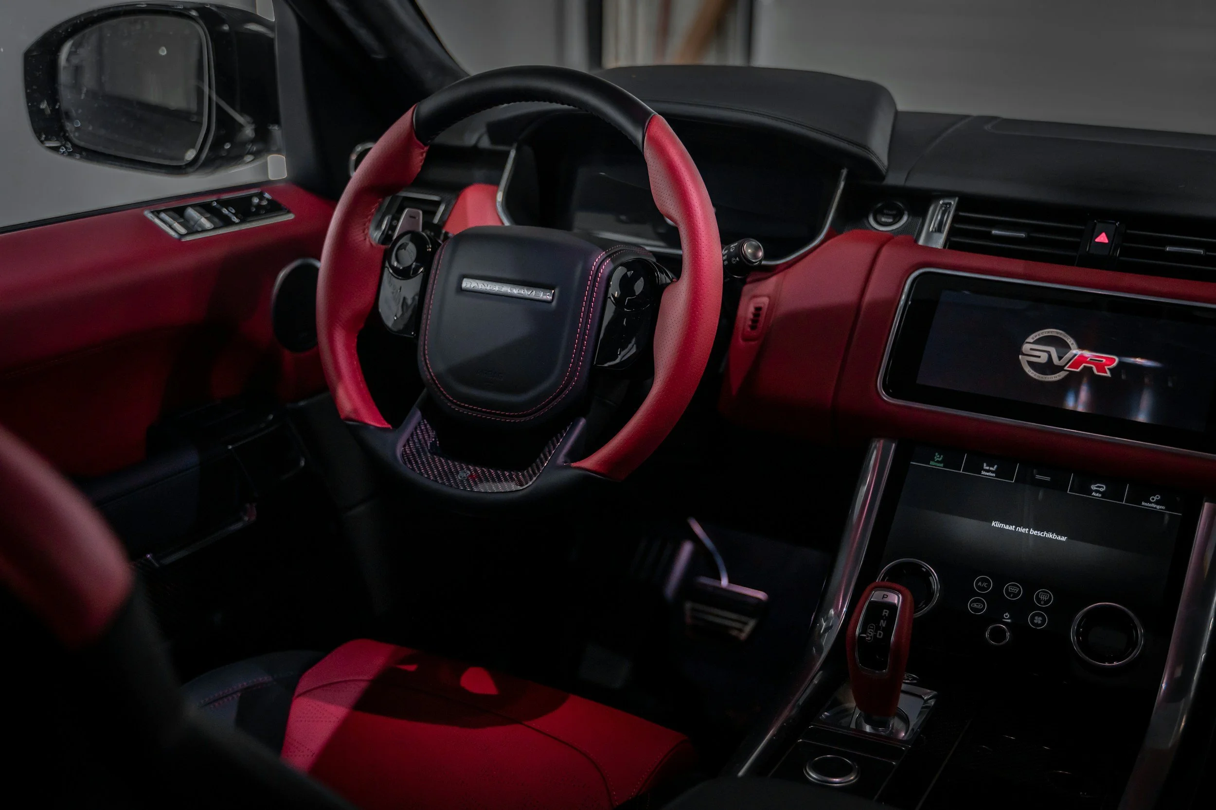 The interior of a car with a red and black color scheme, featuring a steering wheel, dashboard, and digital display showing the SVR logo.