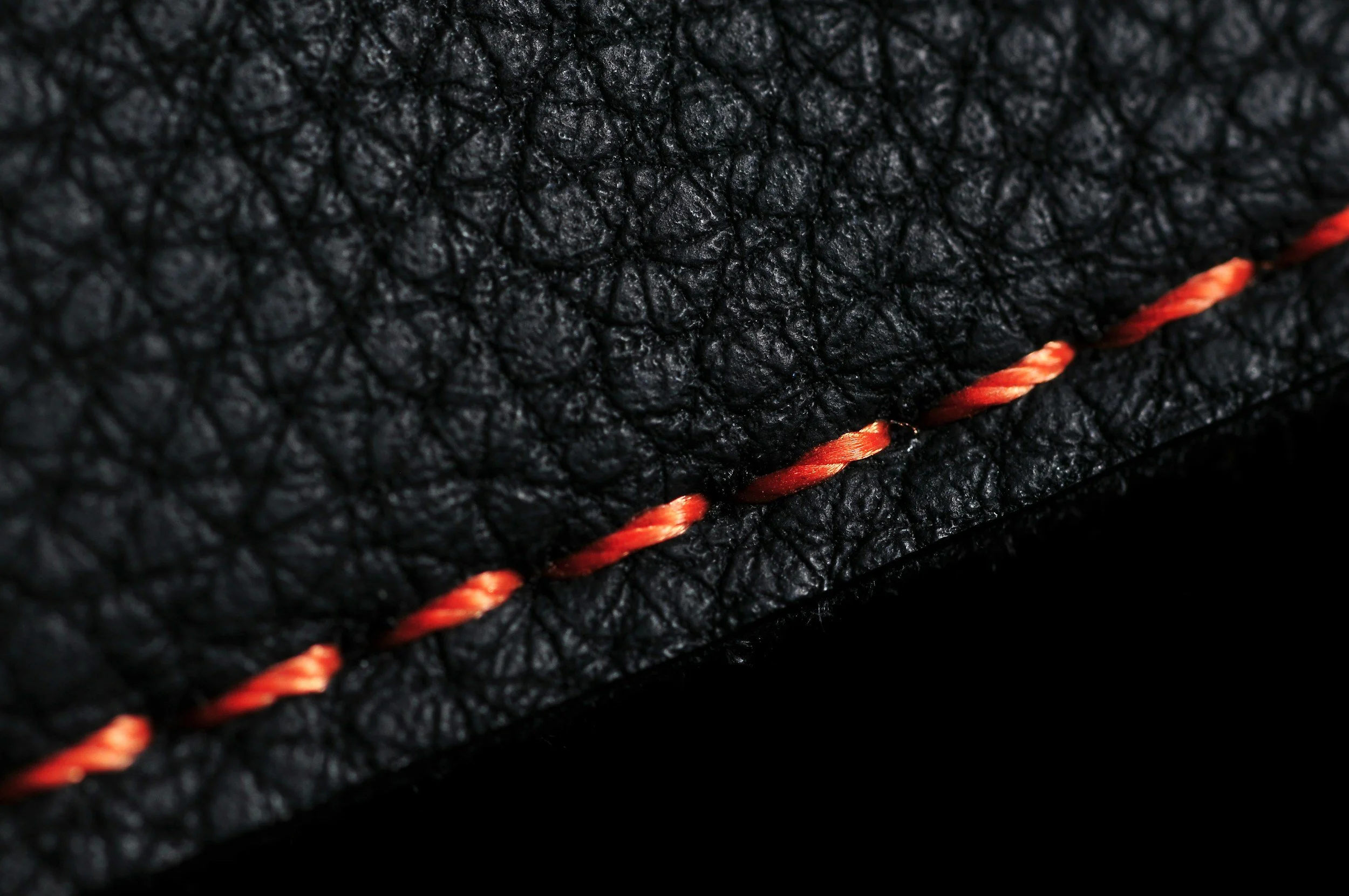 Close-up of black textured leather with red and orange stitched seam.