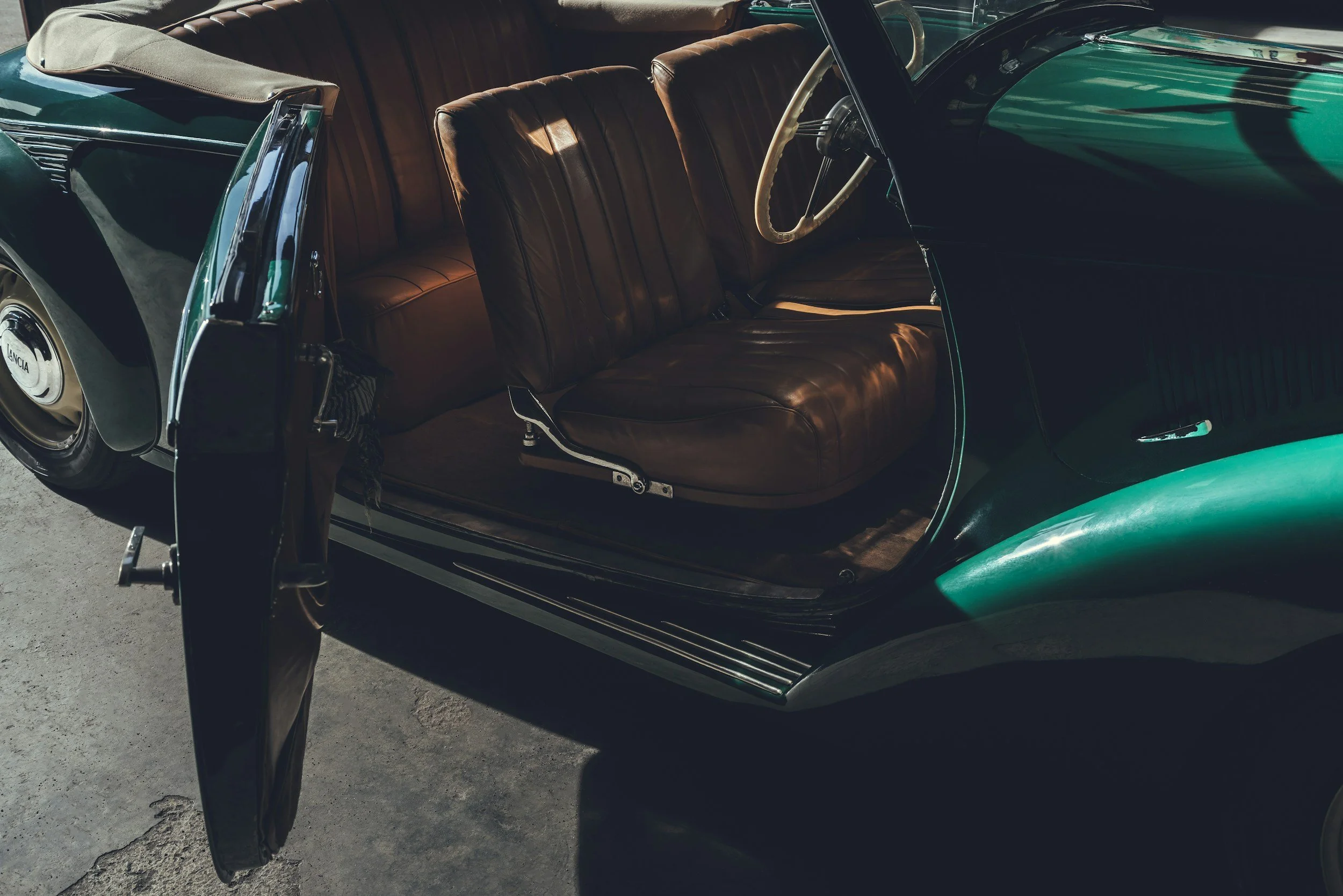 Interior of a vintage car showing brown leather seats and a white steering wheel.