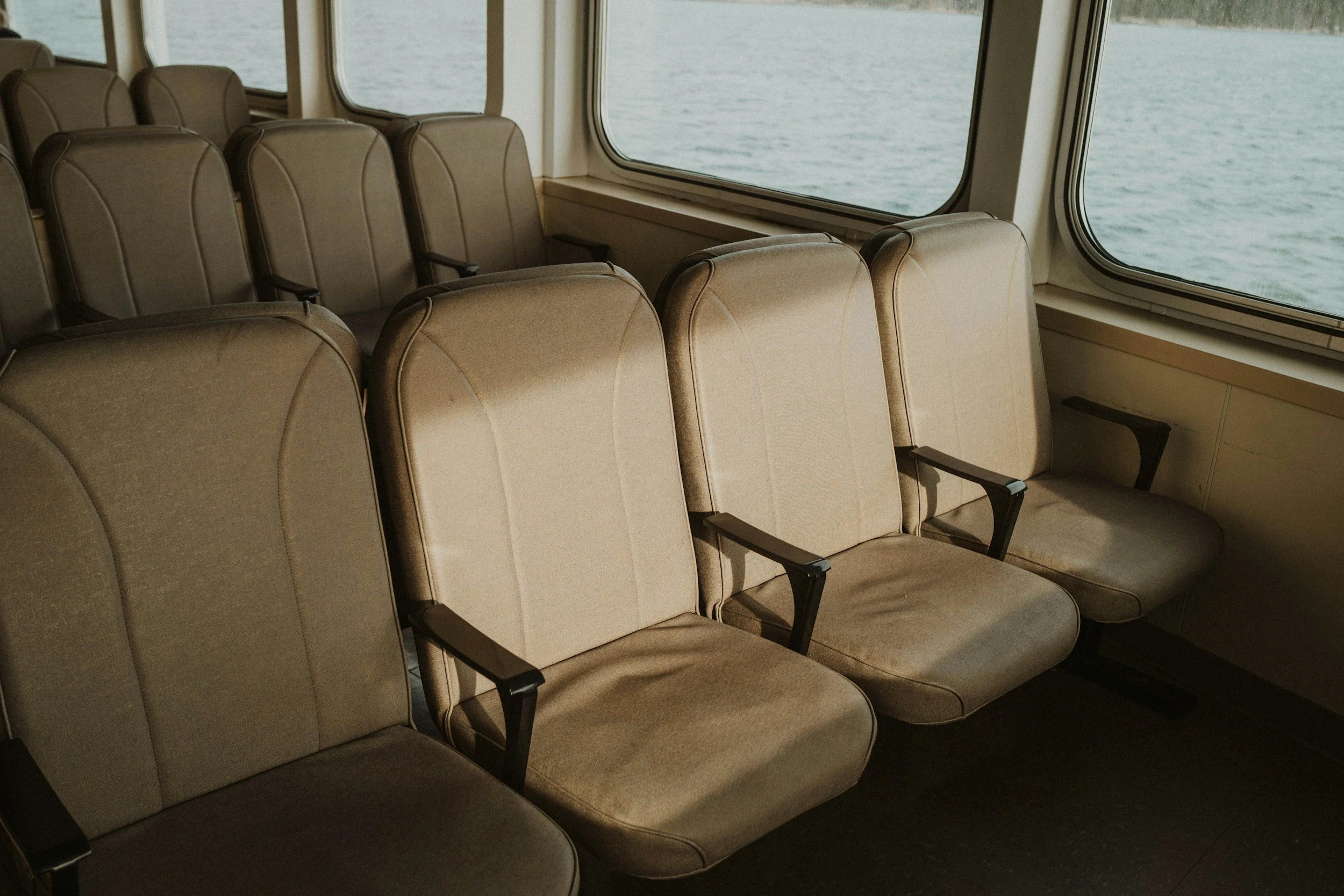 Seats inside a ferry or cruise ship with windows showing water outside.