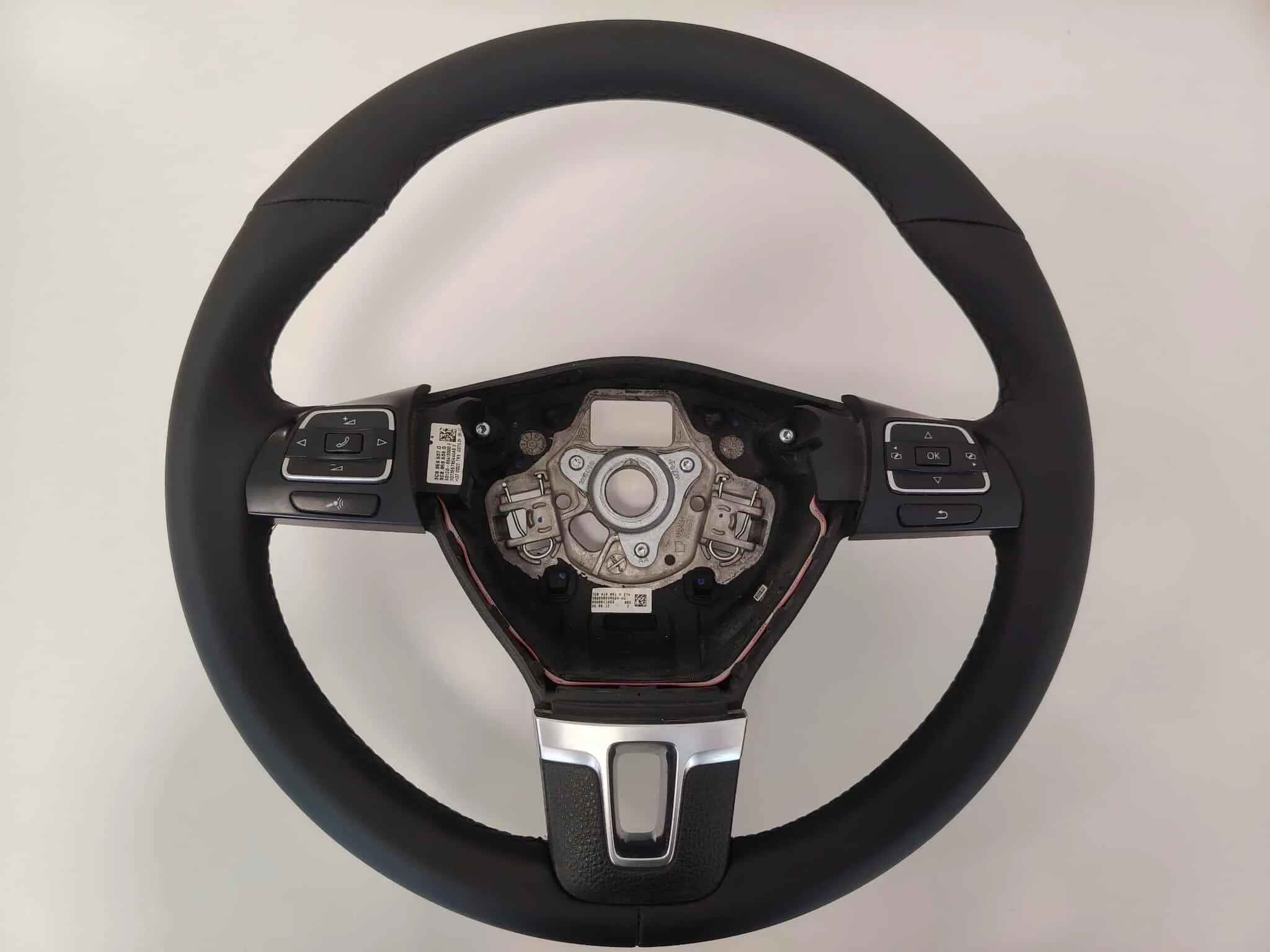 A black car steering wheel with control buttons on both sides, with the central part removed, exposing internal mechanical components and wiring.