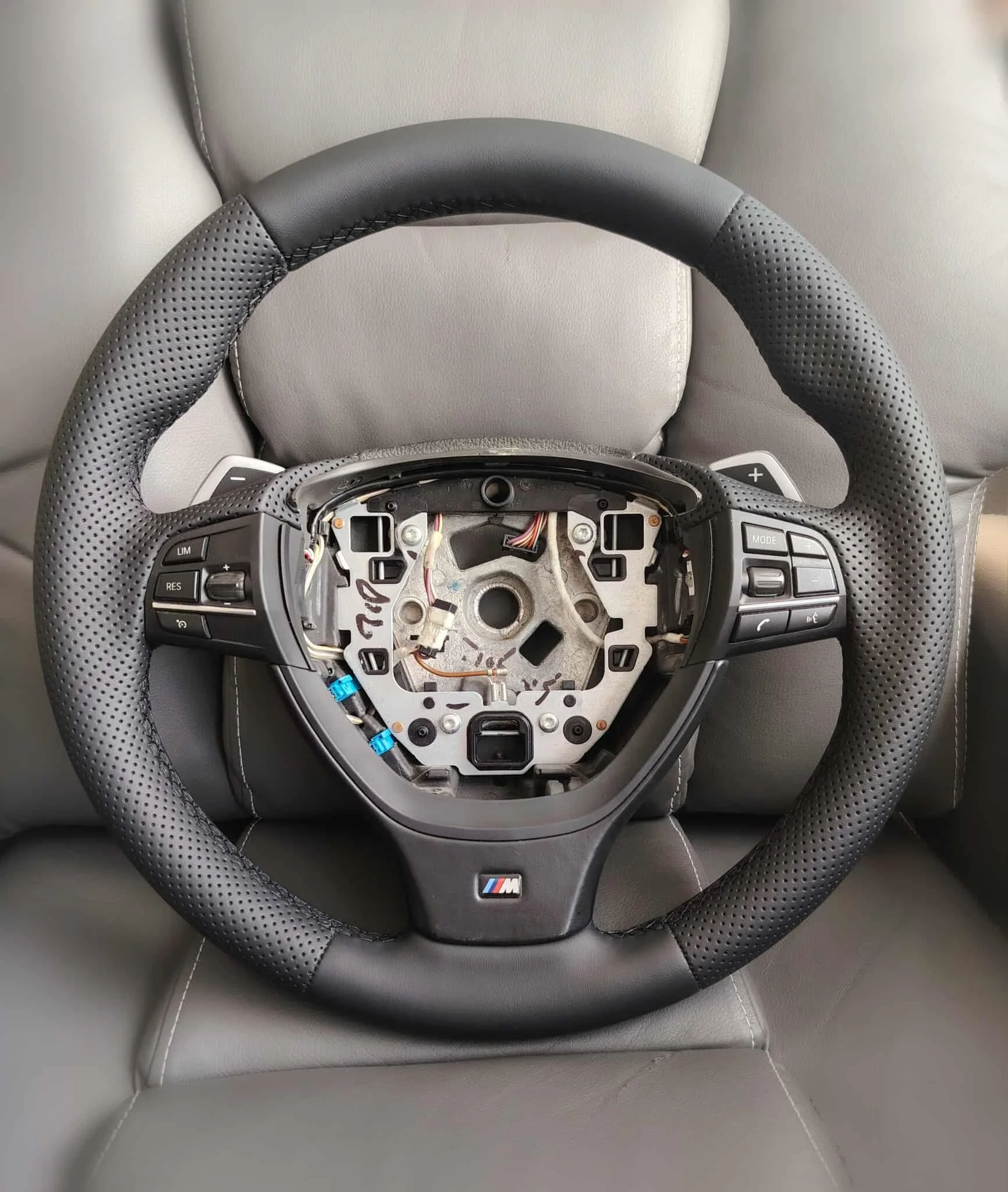 Car steering wheel with buttons and the BMW M logo, removed airbag, sitting on gray car seat.