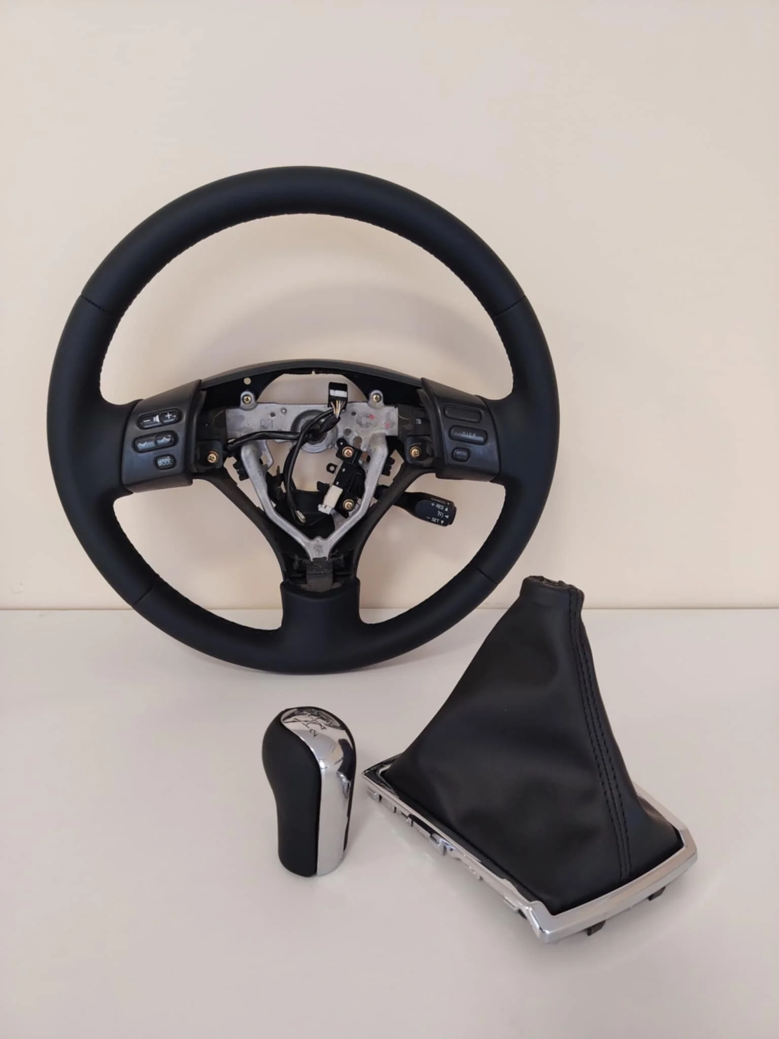 Disassembled car steering wheel, gear shift, and gear shift boot on a white surface.
