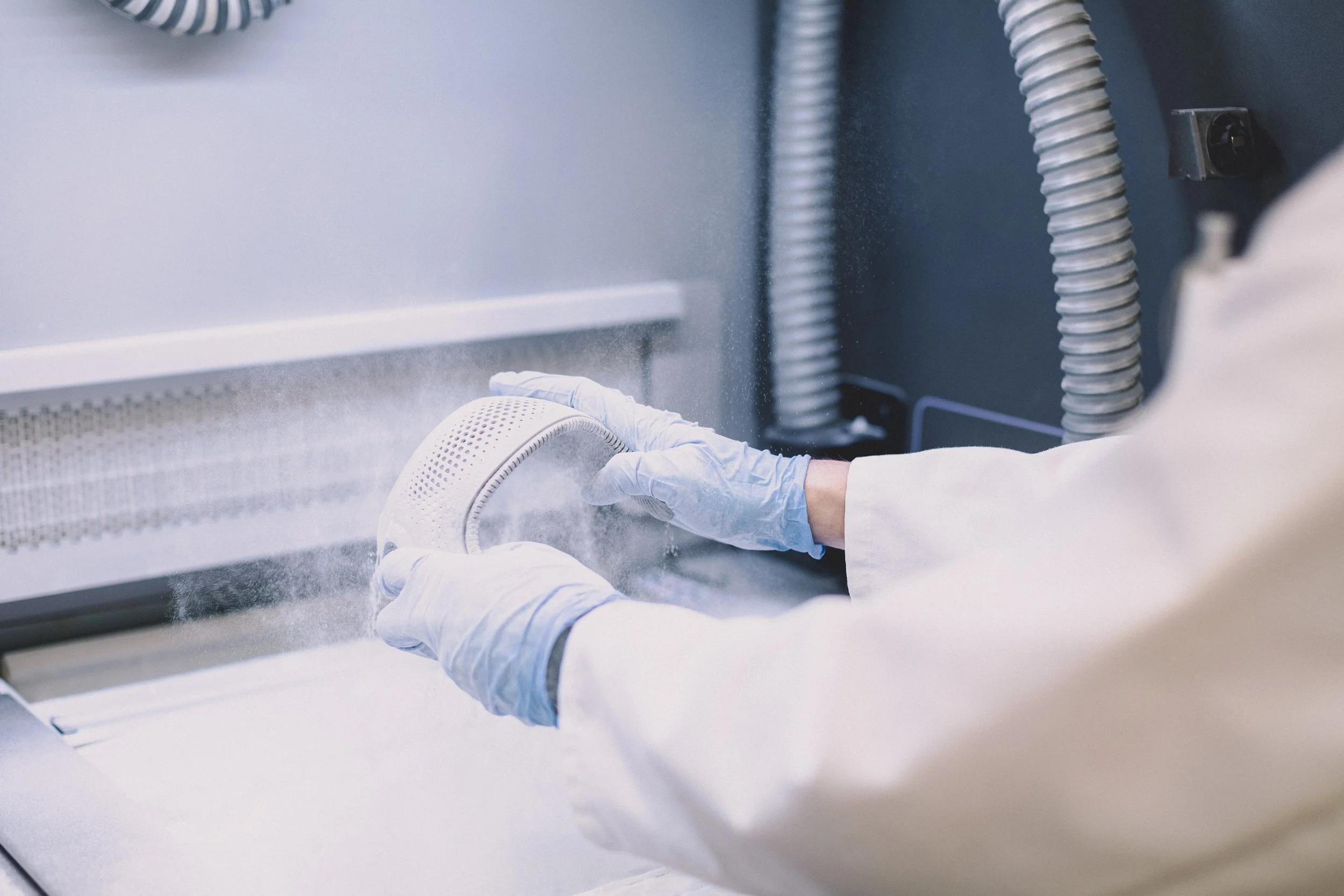 A person wearing gloves and a lab coat cleaning or sterilizing a face mask in a specialized machine.
