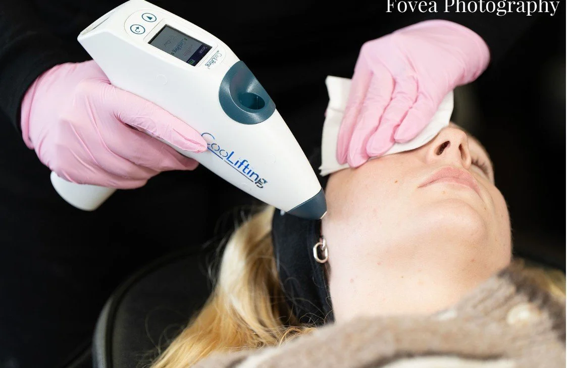 A woman receives a cosmetic treatment on her face using a CoolLifting device, while a technician in pink gloves gently wipes her forehead with a cloth.