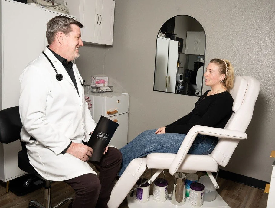 A doctor with a stethoscope talking to a woman sitting in a medical examination chair.