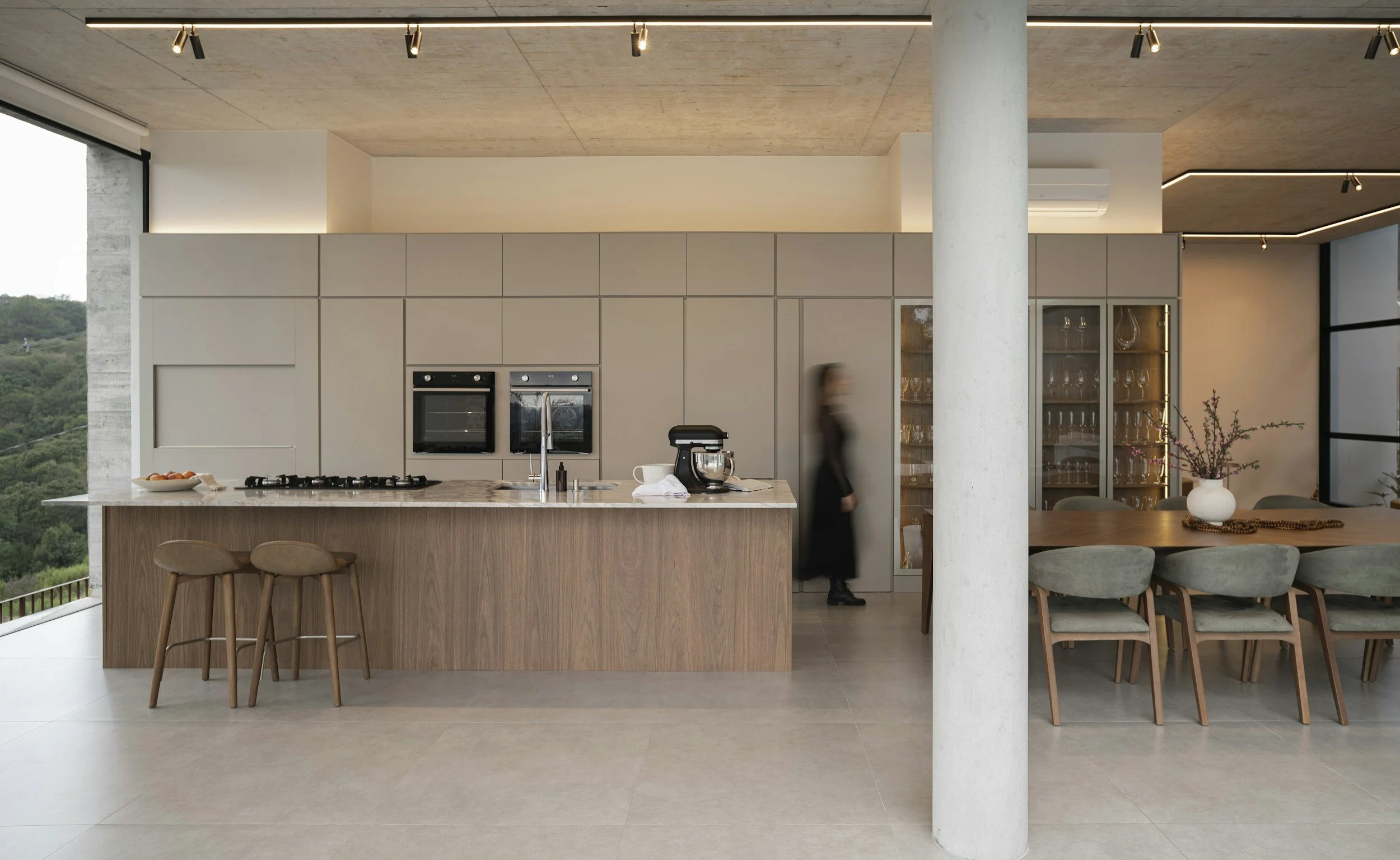 Modern kitchen with beige cabinets, marble island, and a dining area with a large wooden table and gray chairs.