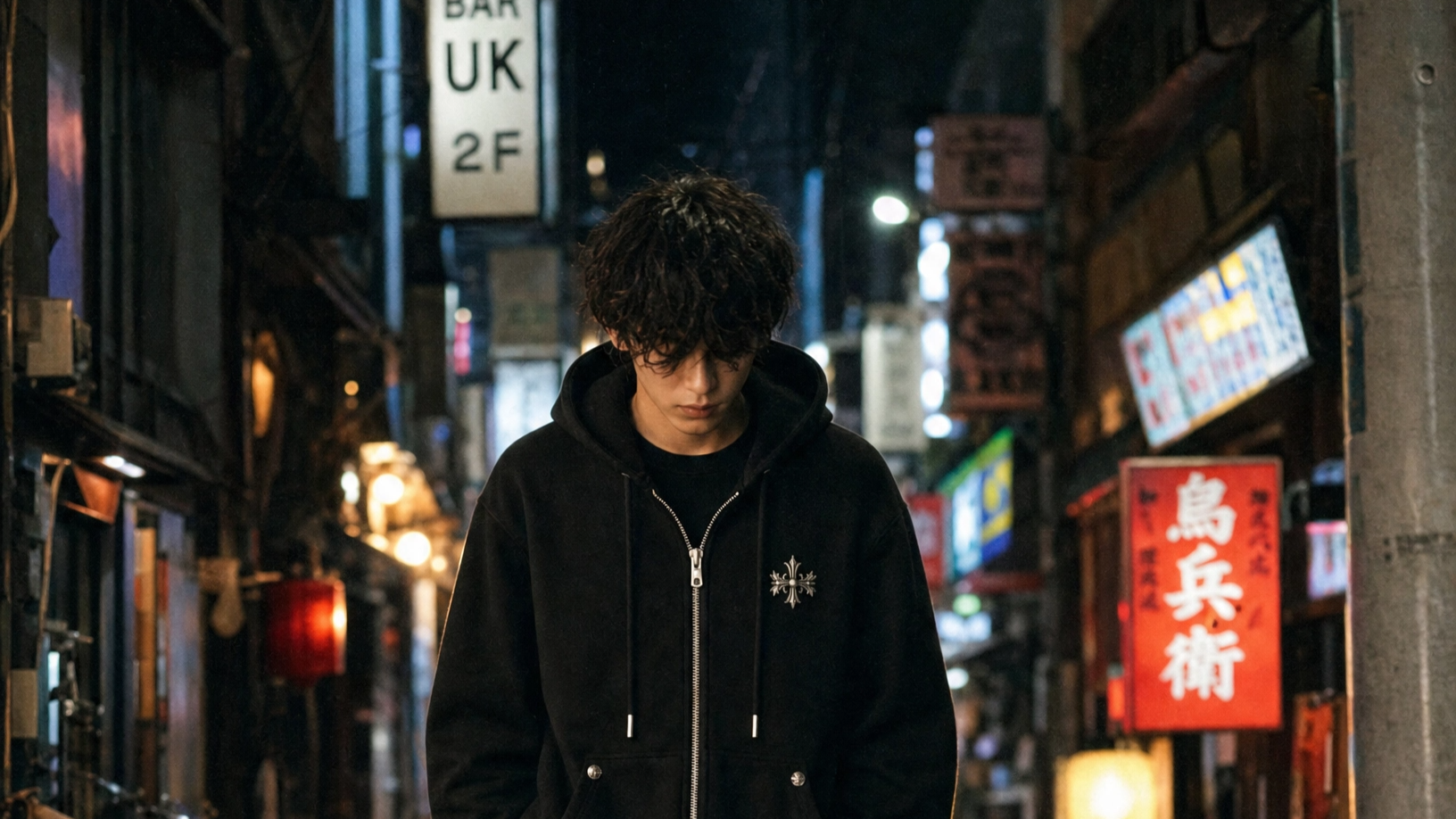 A young person with dark curly hair walking down a wet, neon-lit street at night, wearing black clothing and looking down.