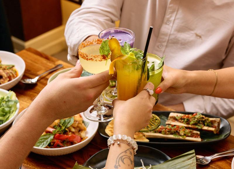 photo of 4 people toasting with cocktails over a table full of Thai dishes at Jumbo Thai
