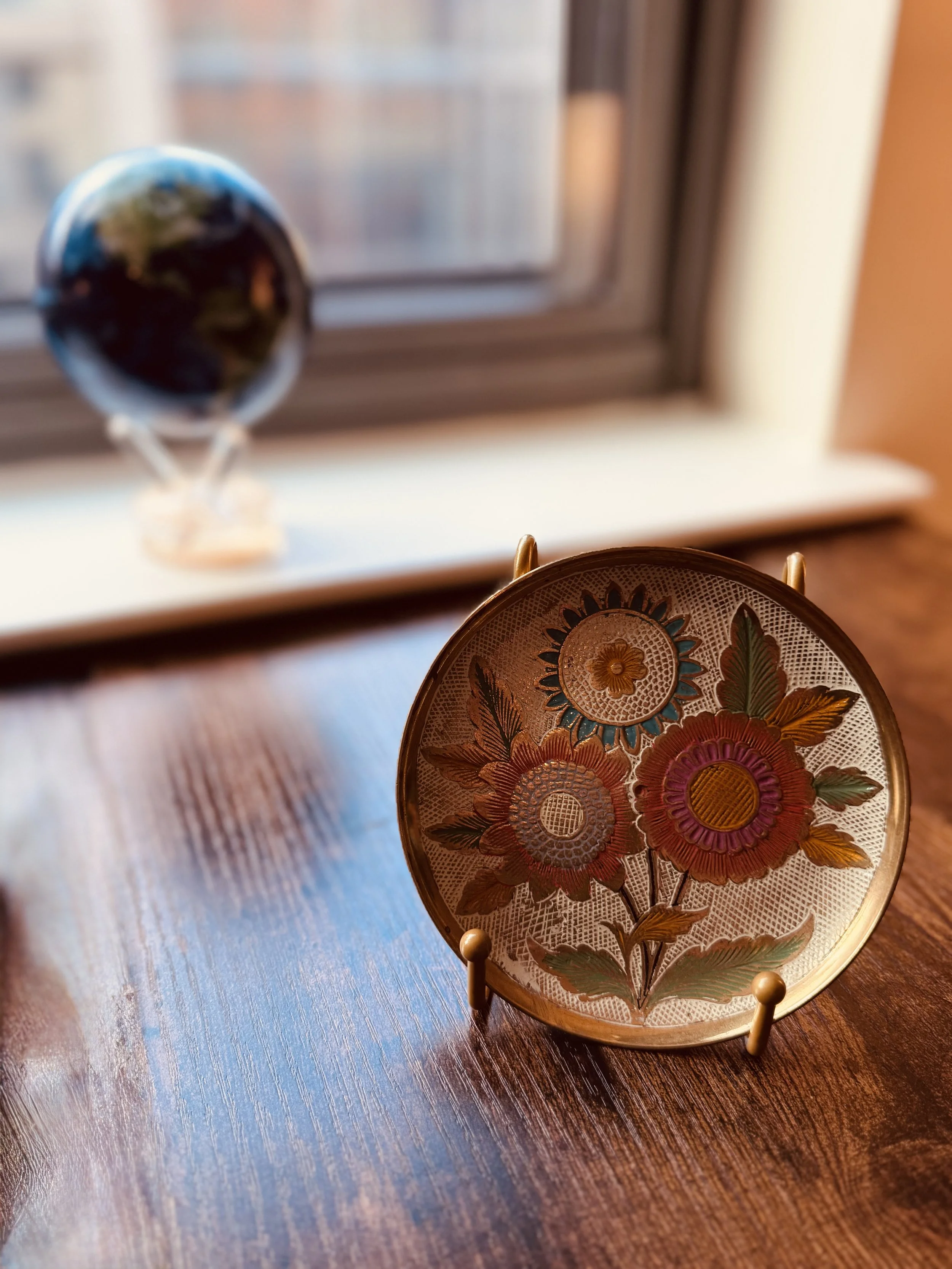 Decorative glass plate with colorful floral pattern placed on a wooden table near a window.