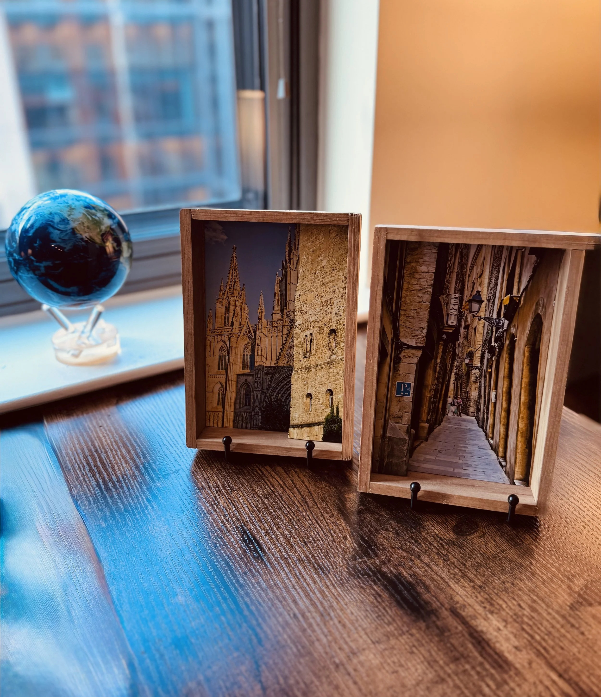 Wooden display boxes with scenic photos of European architecture, a miniature globe, and a window with brown walls.