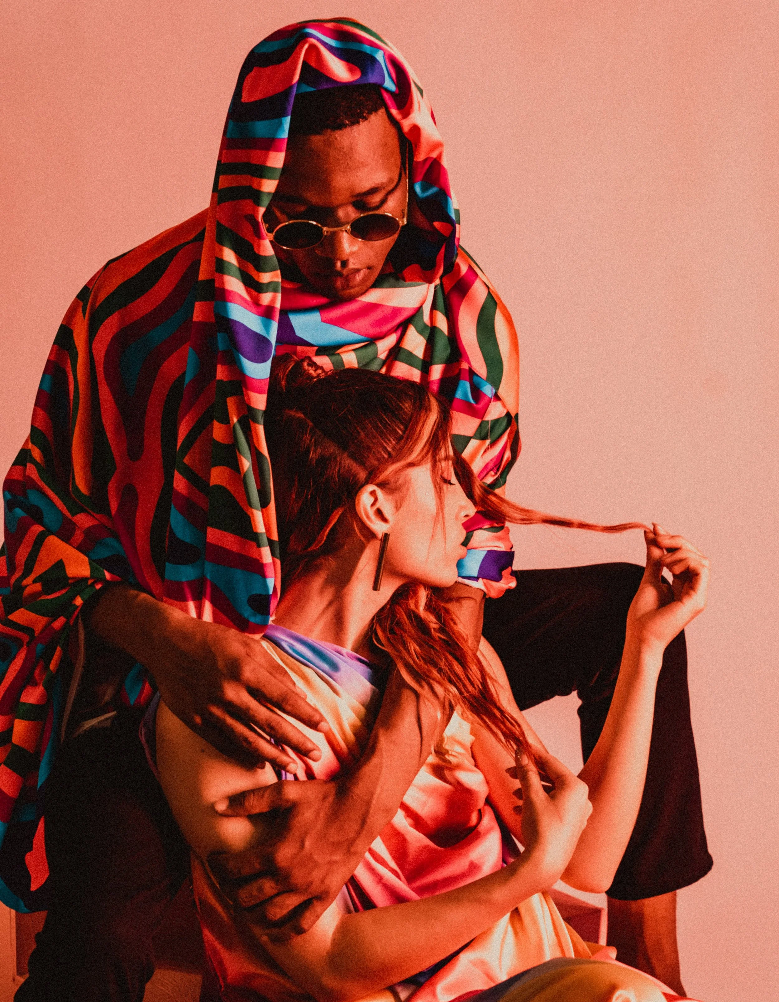 A man and woman with vibrant clothing and accessories posing against a pink background.