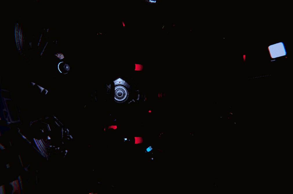 Interior view of a spaceship cockpit with illuminated control panels, screens, and buttons amidst darkness.