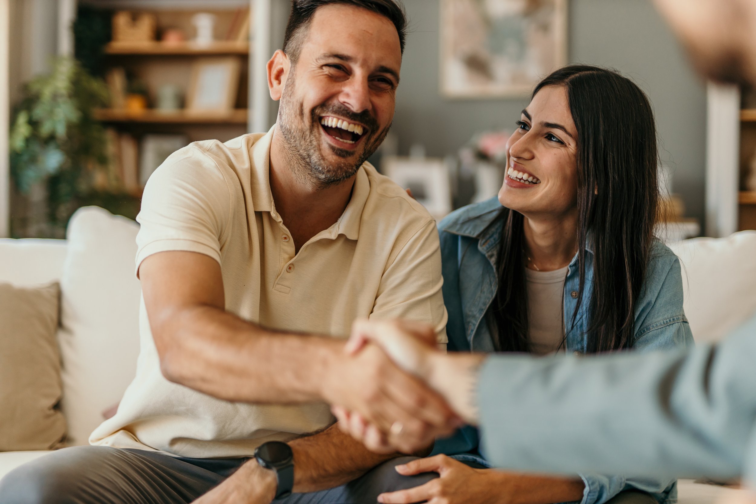 A man and woman smiling and shaking hands in a living room.