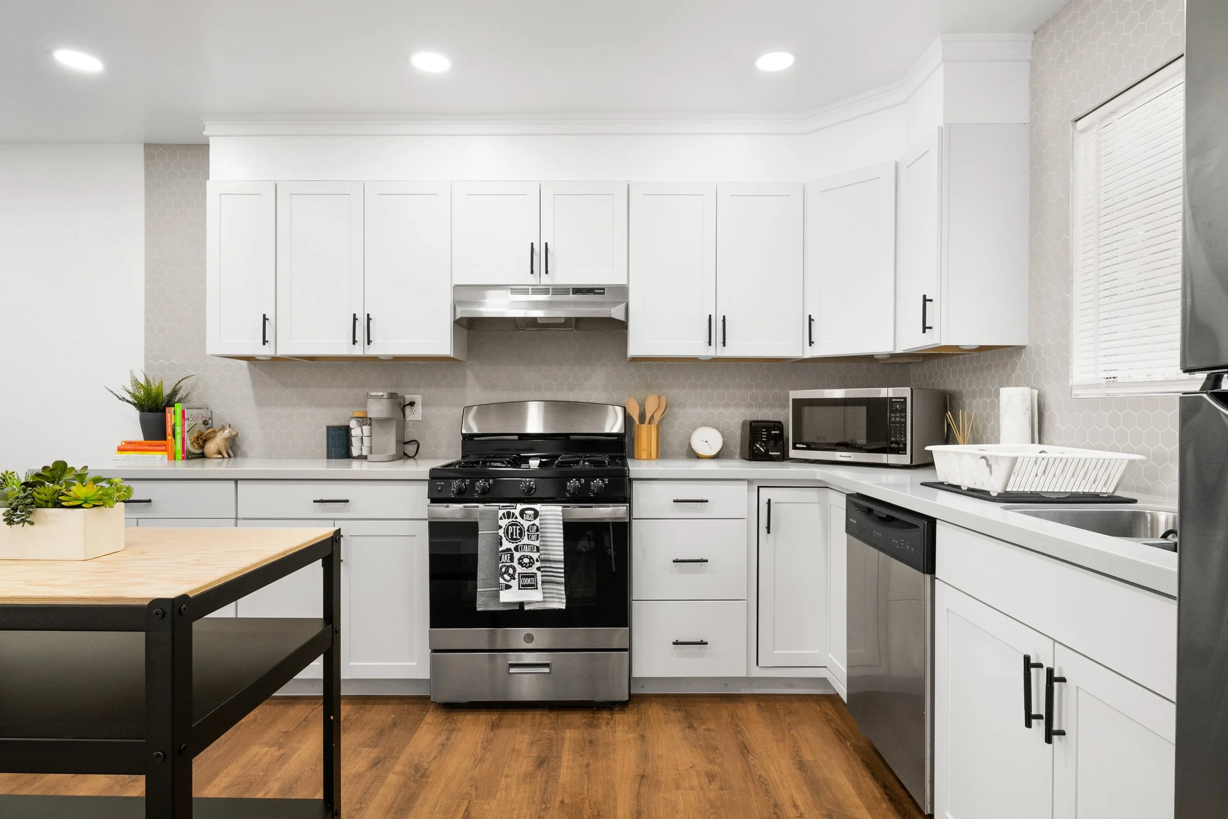 Modern kitchen with white cabinets, stainless steel appliances, a gas stove, microwave, dishwasher, and a window with blinds.