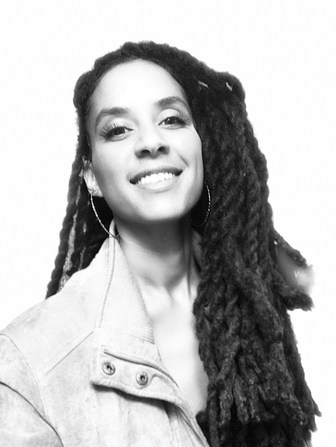 A woman with long, textured dreadlocks smiling in a black and white photo.