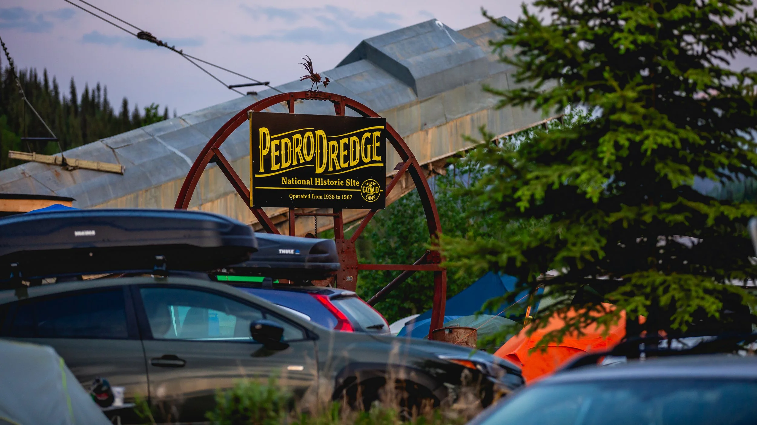 Sign for Pedro Dredge, a National Historic Site, with parked cars and trees in the background.