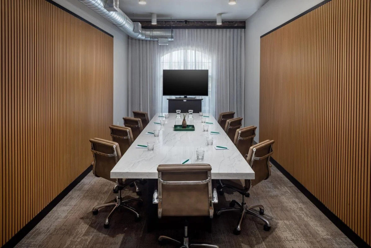 Preston Boardroom set for a meeting with seating for eight, water, notepads, and pens at The Clara Hotel in Plano, Texas.
