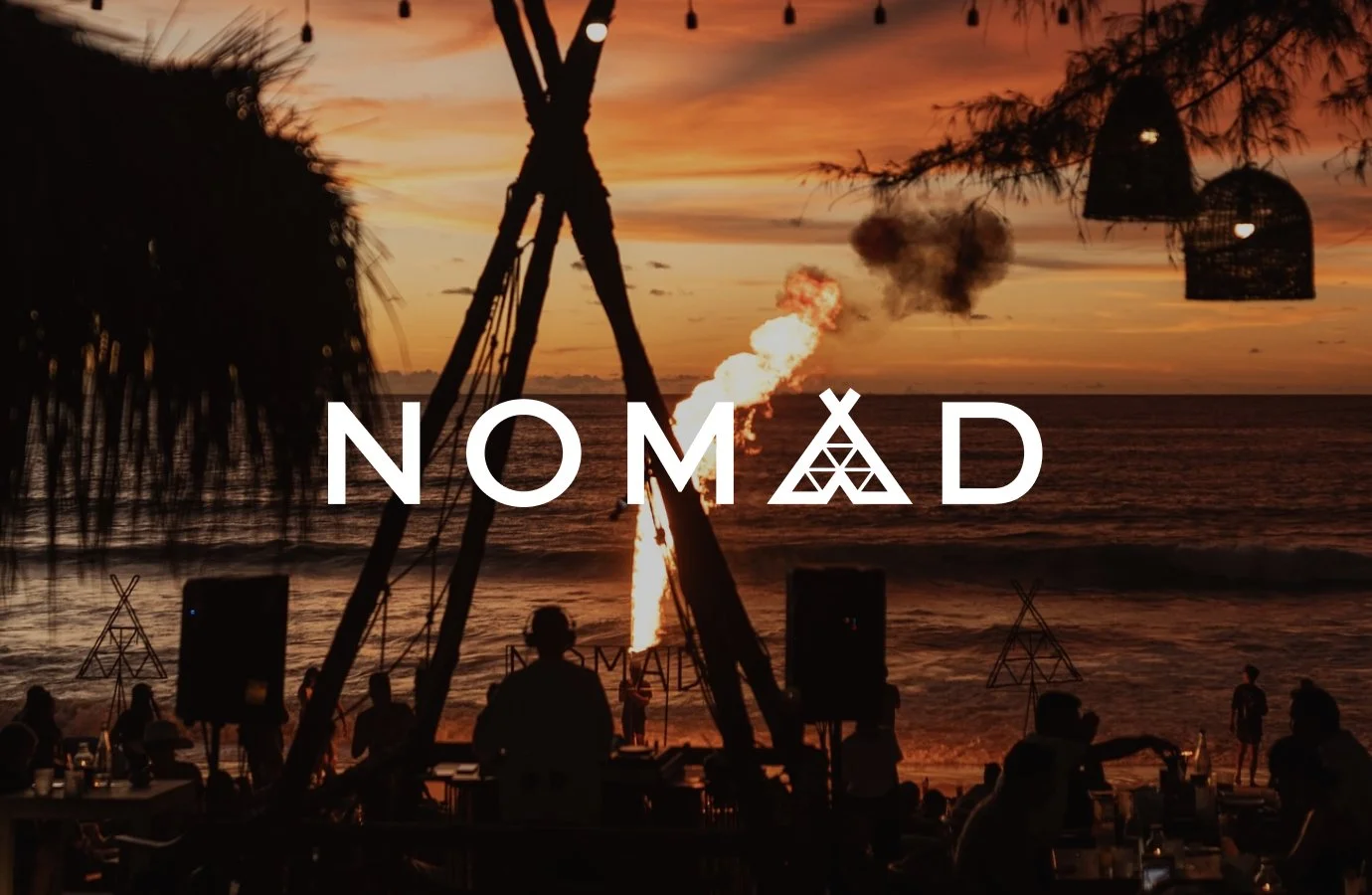 Beach scene at sunset with silhouettes of people, bamboo structures, hanging lanterns, and a fire or explosion in the background, with the word 'NOMAD' across the image.