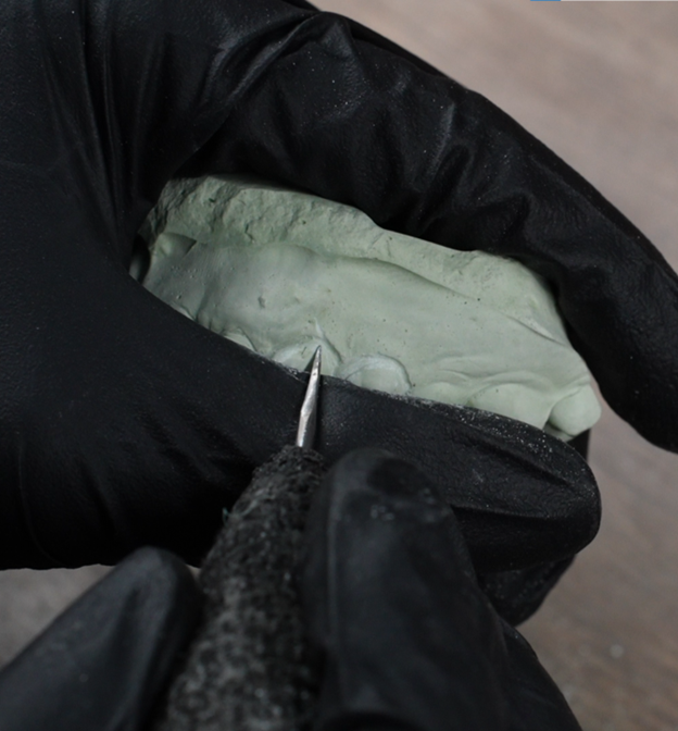 Close-up of a large, ornate gold ring with a sizable square-cut diamond centered on a textured gold band, resting on a dark red cloth.