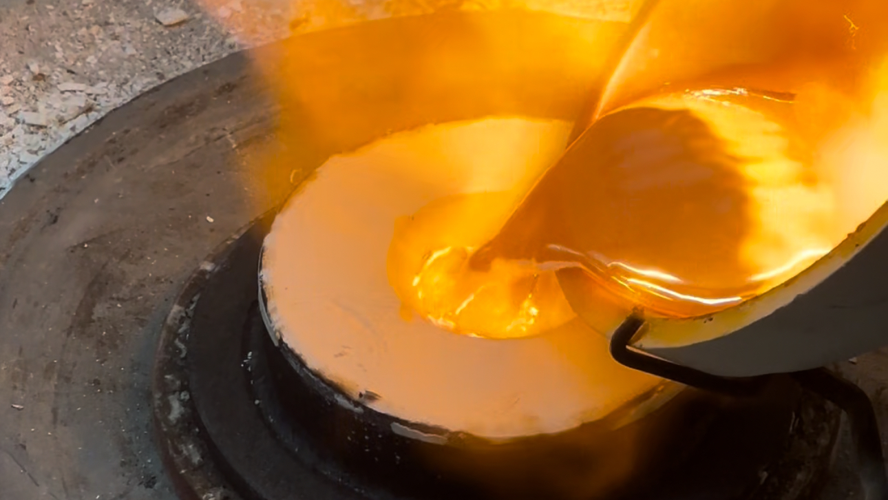 Close-up of a dental technician using a precision tool to work on a gold dental prosthetic with embedded gemstones, wearing a dust-covered glove.