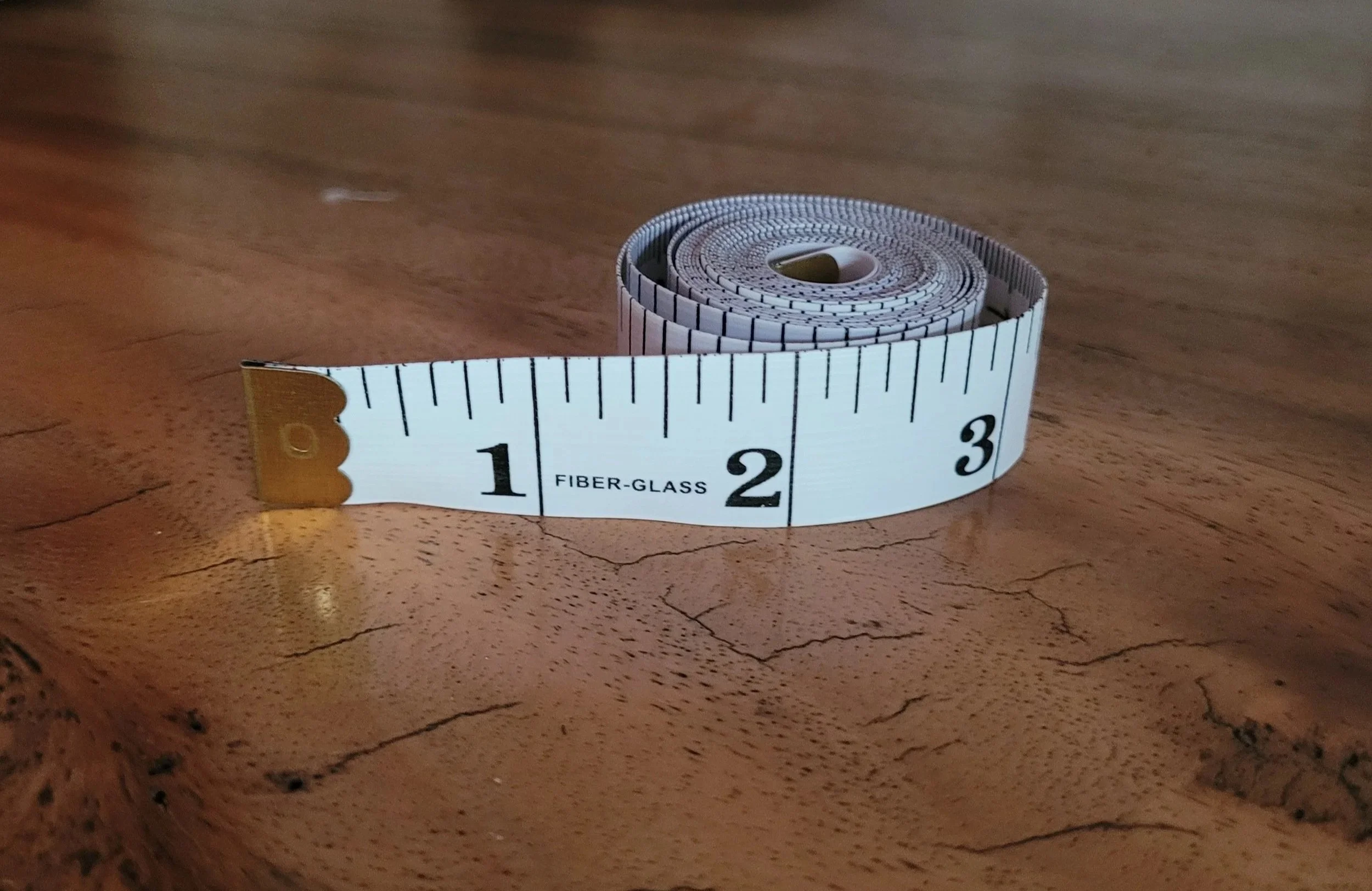 A rolled white fiber-glass measuring tape with black markings partially unrolled on a wooden surface.
