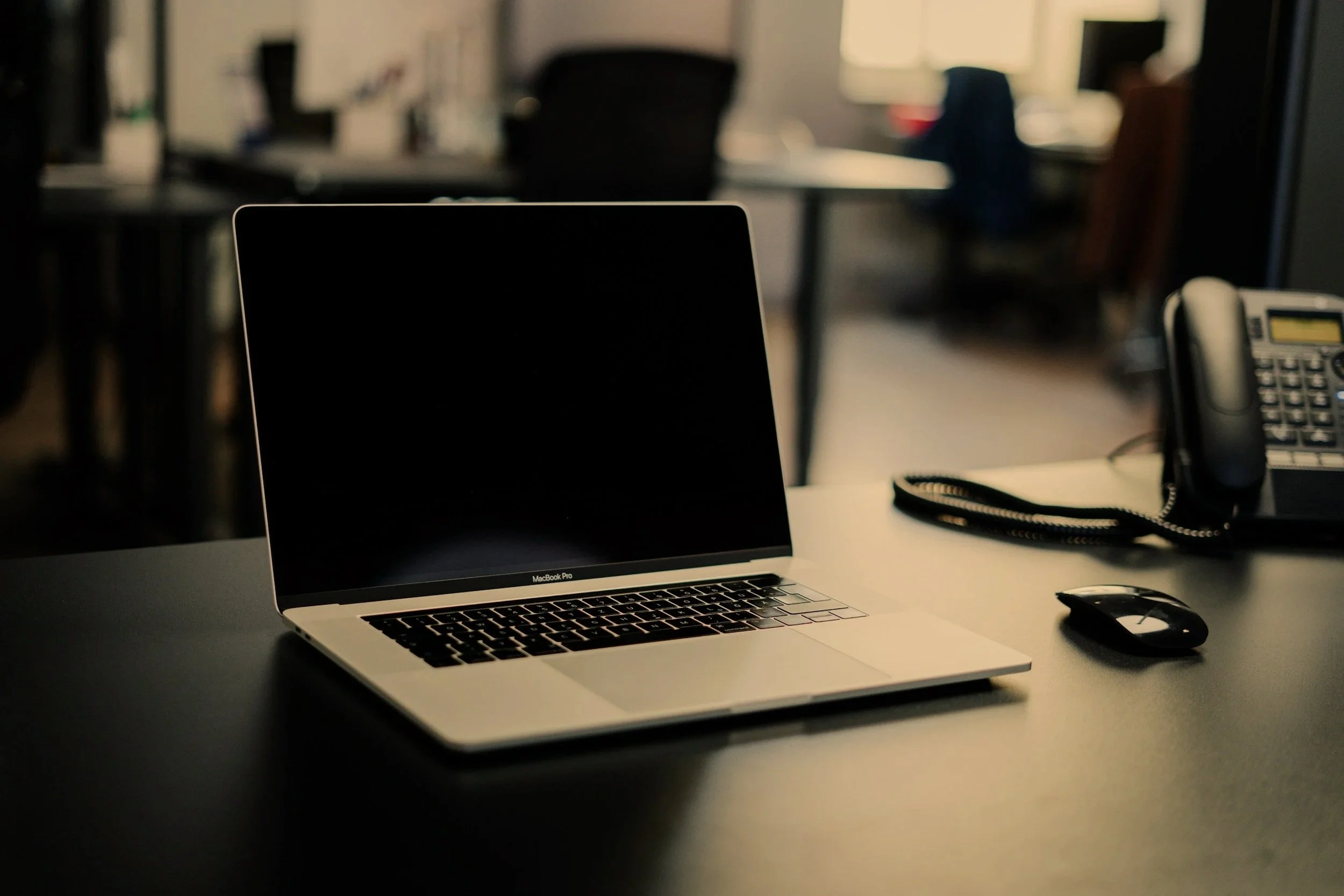 Laptop, mouse, phone, and office supplies on a desk in an office setting.