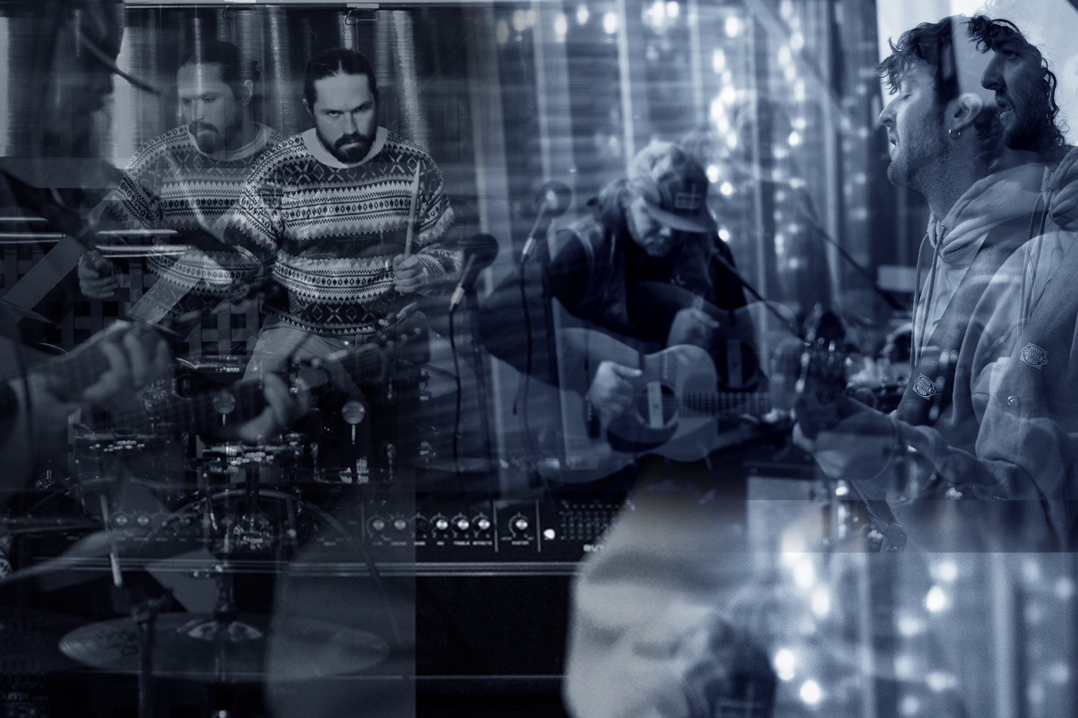 A group of musicians, including guitarists and a drummer, playing music in a cozy, decorated room with Christmas lights, seen through a window with reflections.